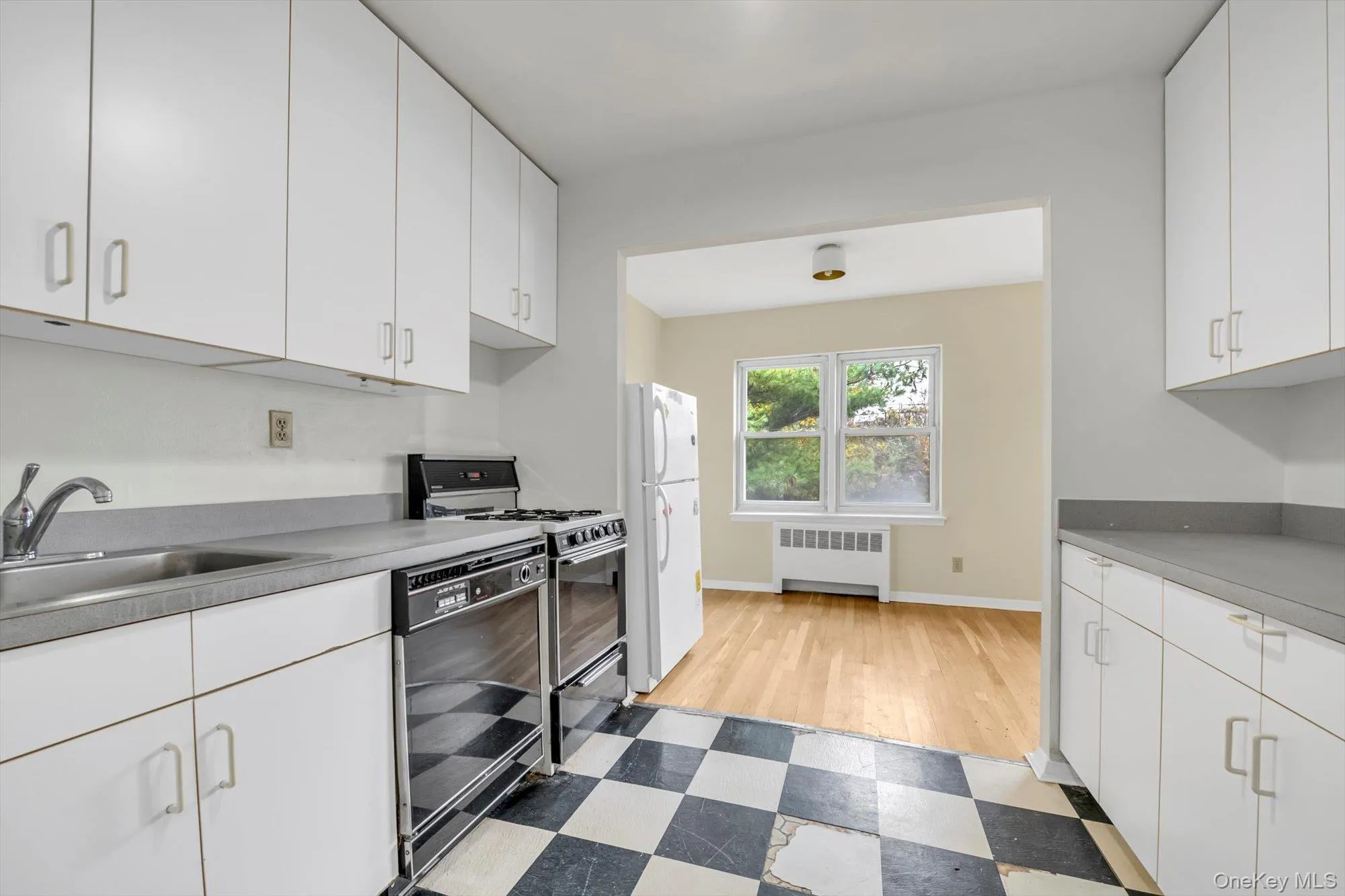 Kitchen featuring white cabinets, gas range oven, radiator heating unit, and freestanding refrigerator Kitchen featuring white cabinets, gas range oven, radiator heating unit, and freestanding refrigerator