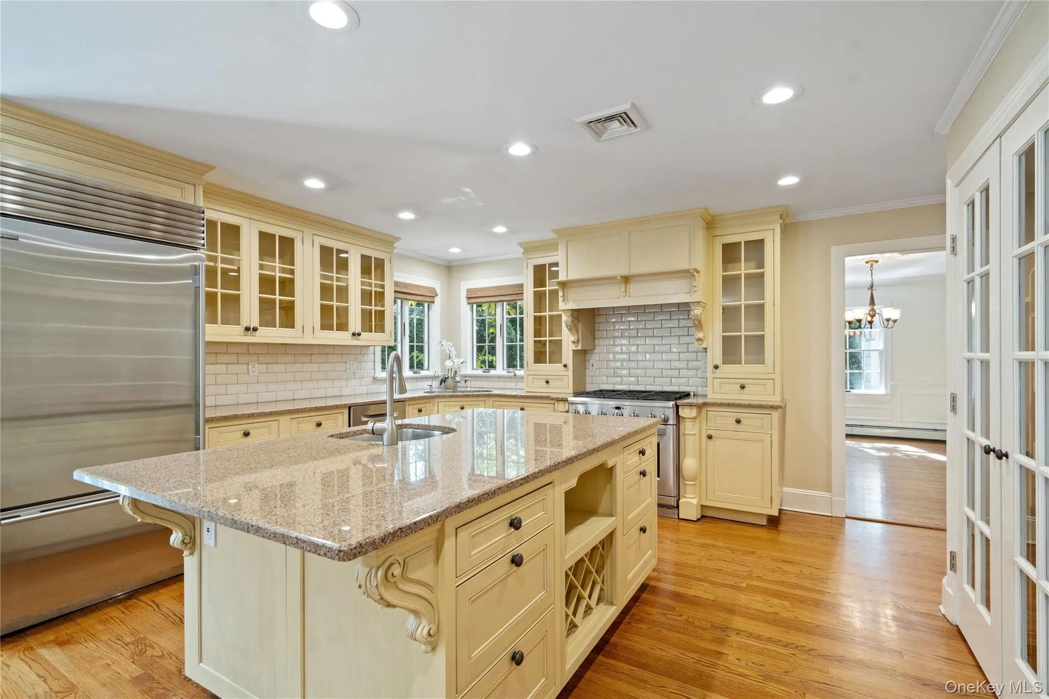 Kitchen with glass insert cabinets, appliances with stainless steel finishes, ornamental molding, light stone counters, and light wood finished floors Kitchen with glass insert cabinets, appliances with stainless steel finishes, ornamental molding, light stone counters, and light wood finished floors