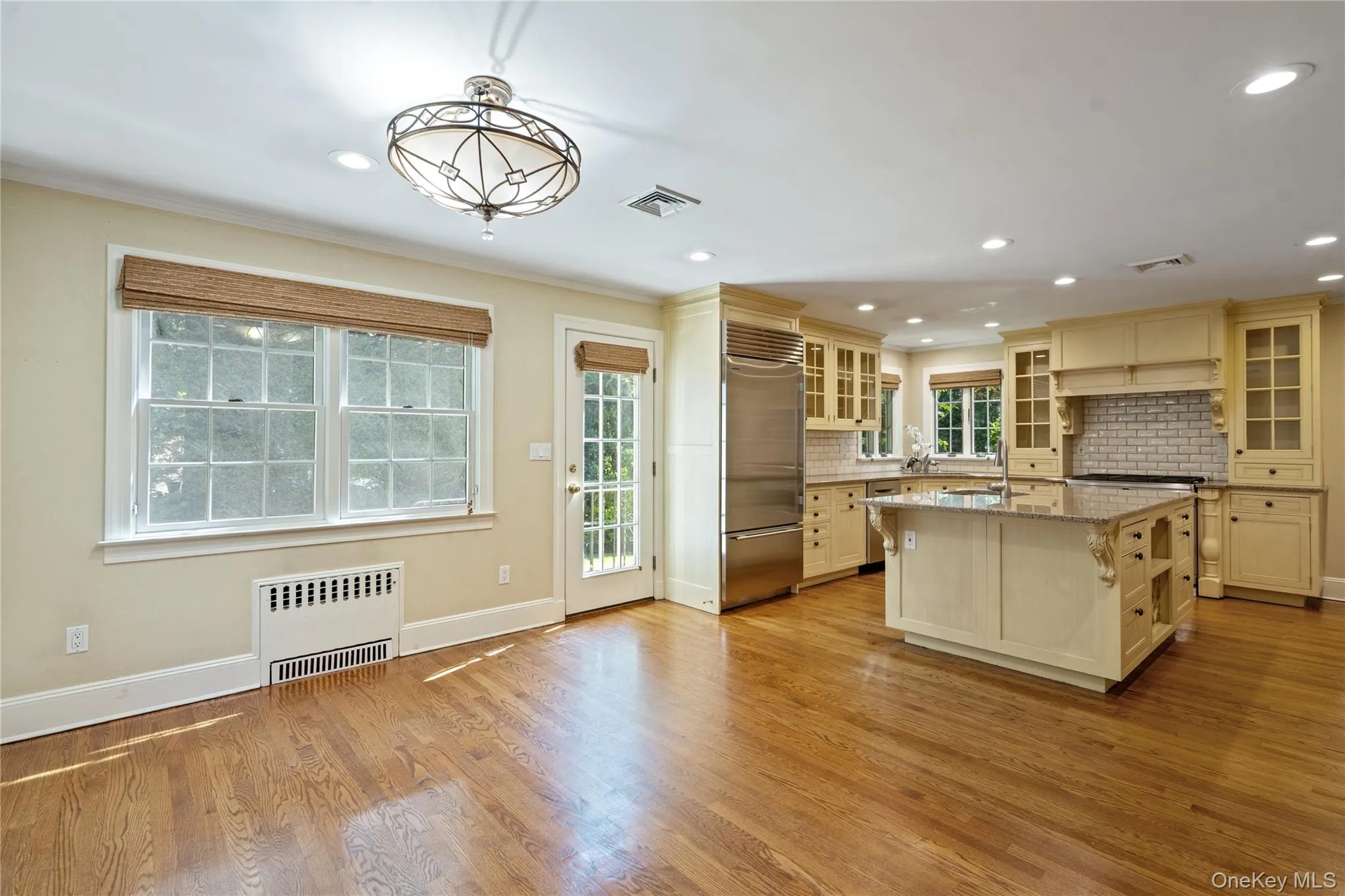 Kitchen with glass insert cabinets, radiator heating unit, stainless steel built in fridge, light stone countertops, and decorative light fixtures Kitchen with glass insert cabinets, radiator heating unit, stainless steel built in fridge, light stone countertops, and decorative light fixtures