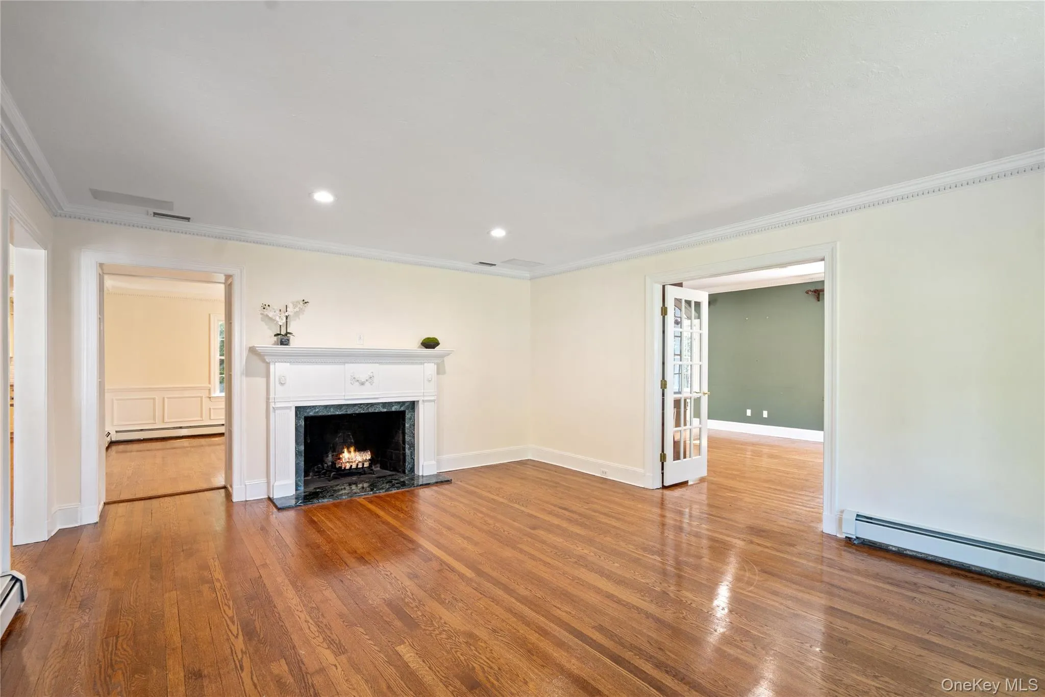 Unfurnished living room with ornamental molding, hardwood / wood-style floors, a premium fireplace, recessed lighting, and baseboard heating Unfurnished living room with ornamental molding, hardwood / wood-style floors, a premium fireplace, recessed lighting, and baseboard heating