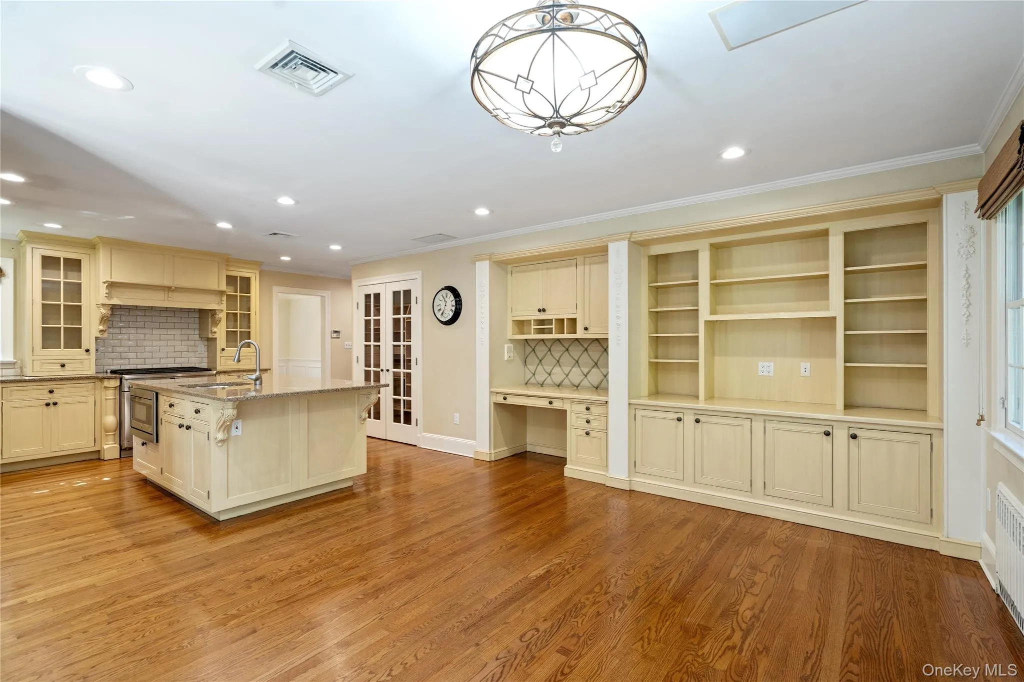 Kitchen with built in study area, backsplash, light wood-style floors, a center island with sink, and light stone counters Kitchen with built in study area, backsplash, light wood-style floors, a center island with sink, and light stone counters