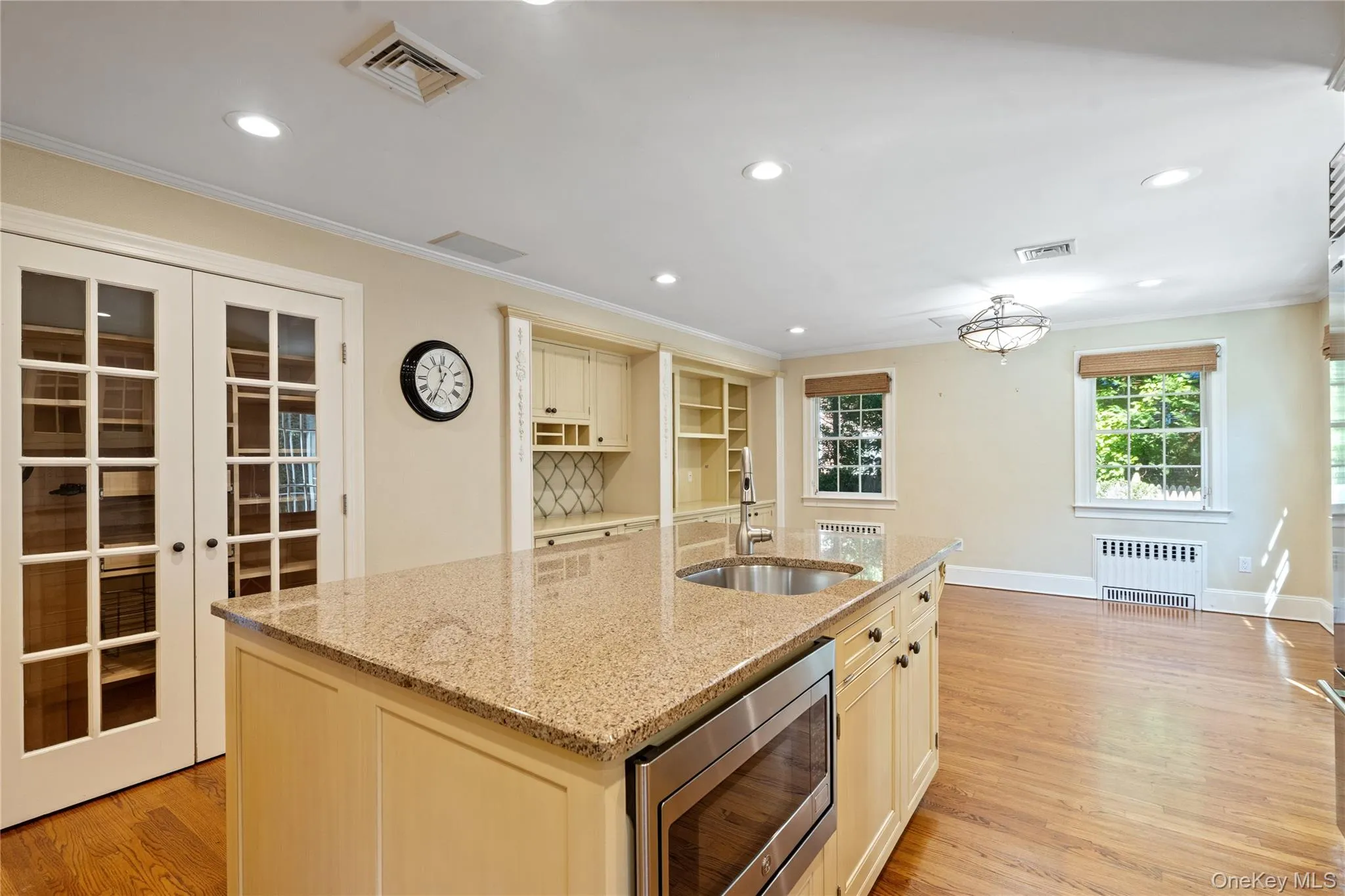 Kitchen with stainless steel microwave, a kitchen island with sink, light wood finished floors, light stone countertops, and crown molding Kitchen with stainless steel microwave, a kitchen island with sink, light wood finished floors, light stone countertops, and crown molding