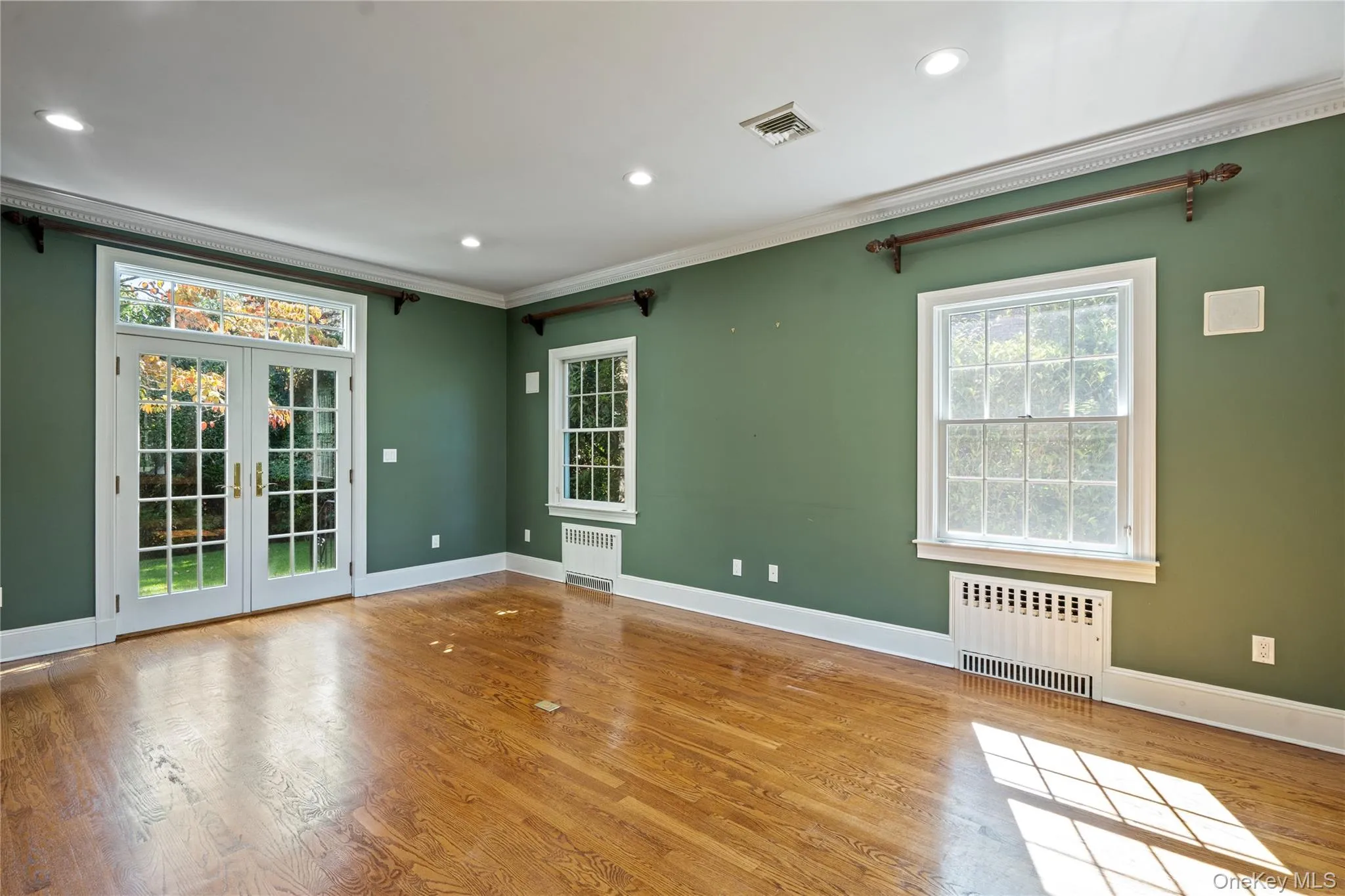 Empty room featuring french doors, radiator heating unit, wood finished floors, crown molding, and recessed lighting Empty room featuring french doors, radiator heating unit, wood finished floors, crown molding, and recessed lighting