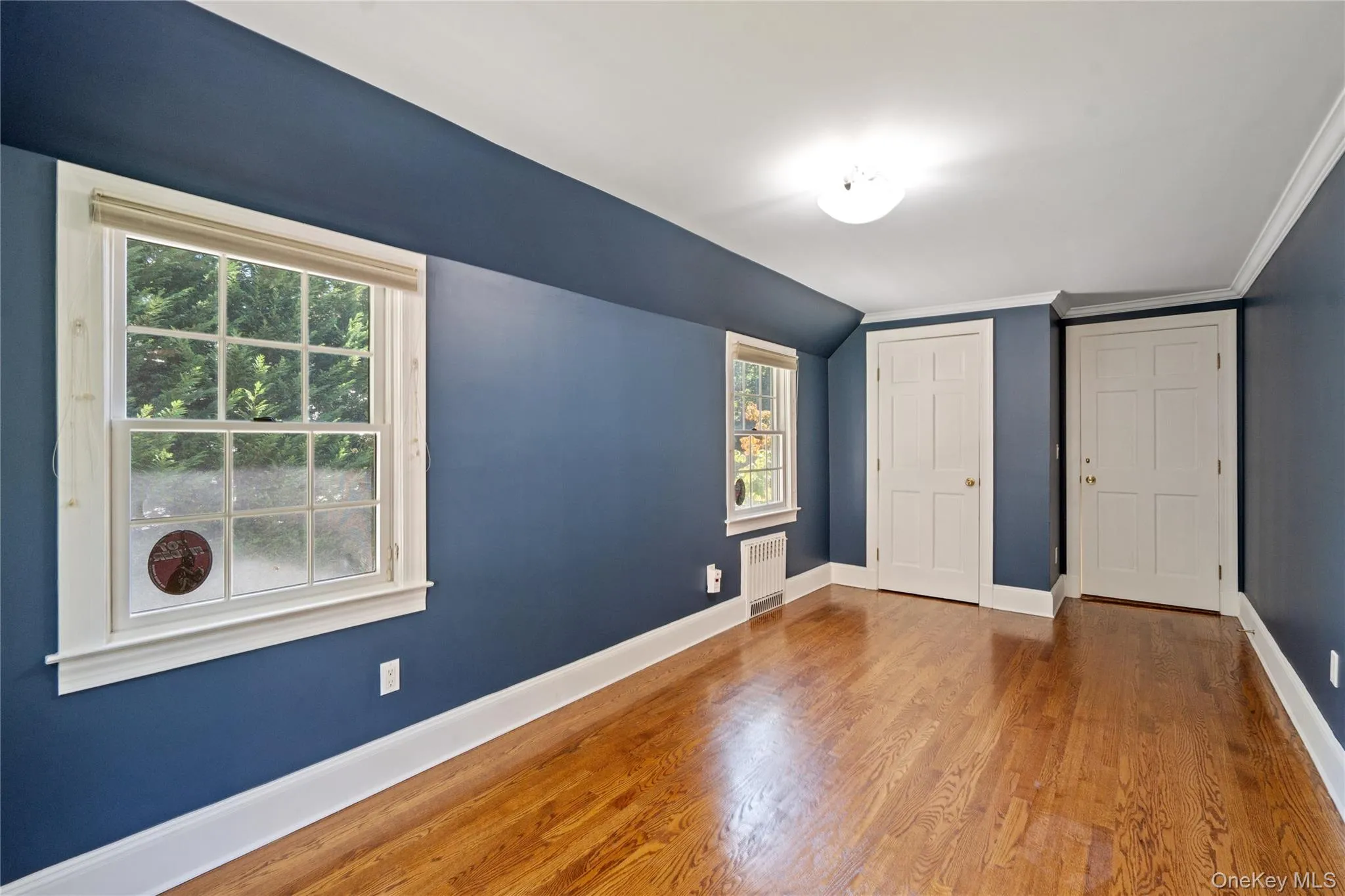 Unfurnished bedroom featuring wood finished floors, radiator heating unit, a closet, lofted ceiling, and crown molding Unfurnished bedroom featuring wood finished floors, radiator heating unit, a closet, lofted ceiling, and crown molding