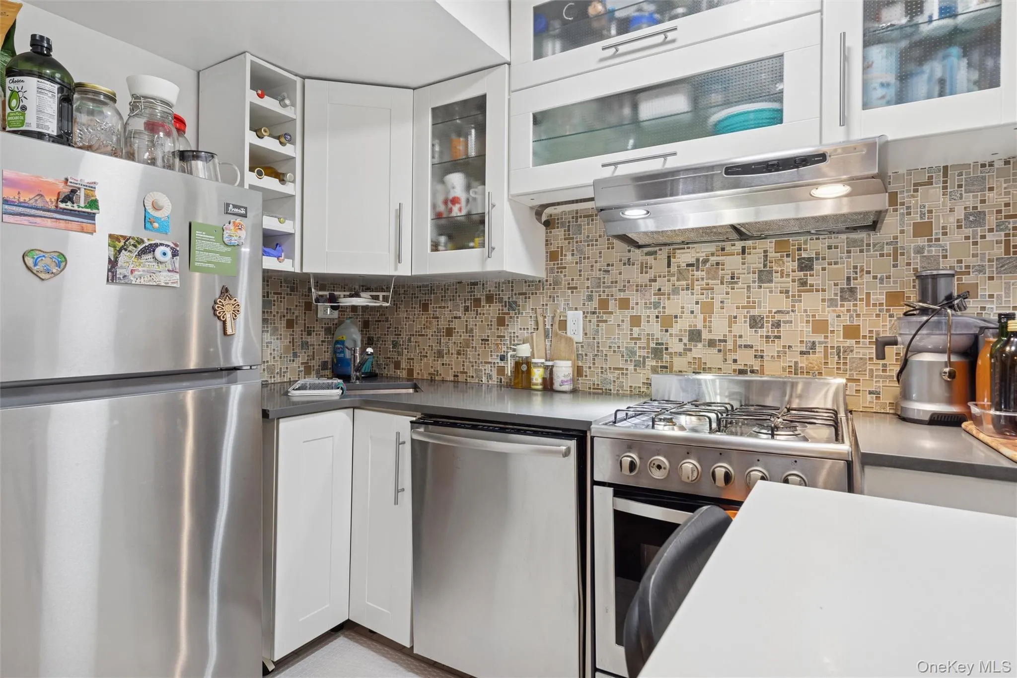 Kitchen with appliances with stainless steel finishes, white cabinets, extractor fan, dark countertops, and tasteful backsplash Kitchen with appliances with stainless steel finishes, white cabinets, extractor fan, dark countertops, and tasteful backsplash