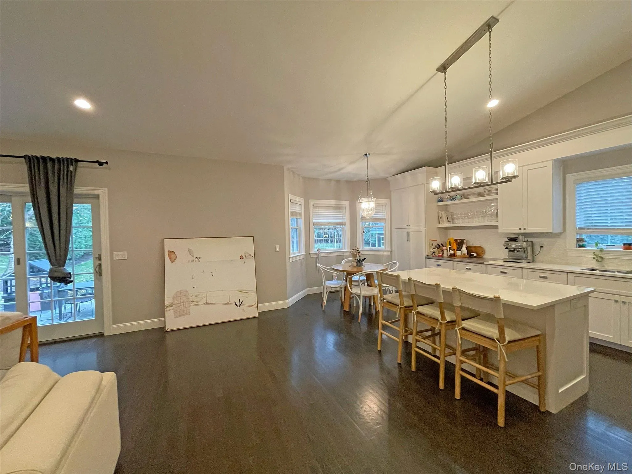 Kitchen with white cabinetry, decorative light fixtures, dark wood-type flooring, and a kitchen island Kitchen with white cabinetry, decorative light fixtures, dark wood-type flooring, and a kitchen island