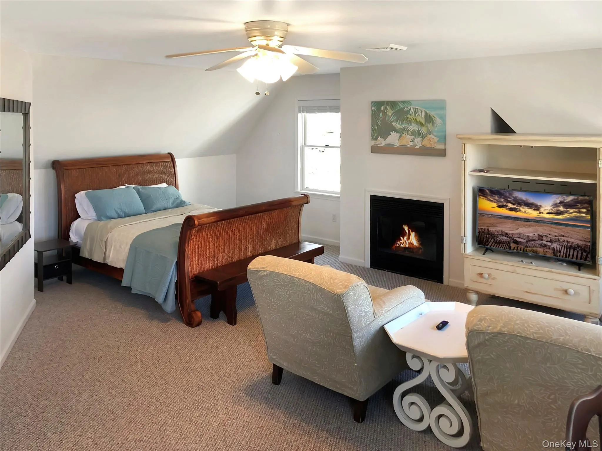 Bedroom featuring carpet flooring, vaulted ceiling, ceiling fan, and a warm lit fireplace Bedroom featuring carpet flooring, vaulted ceiling, ceiling fan, and a warm lit fireplace