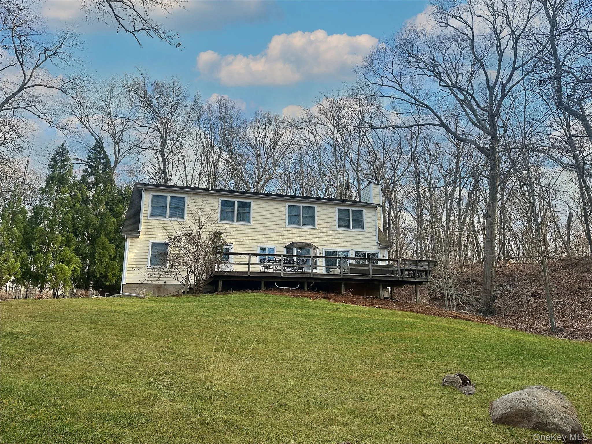 Rear view of house featuring a deck, a yard, a chimney, and view of wooded area Rear view of house featuring a deck, a yard, a chimney, and view of wooded area