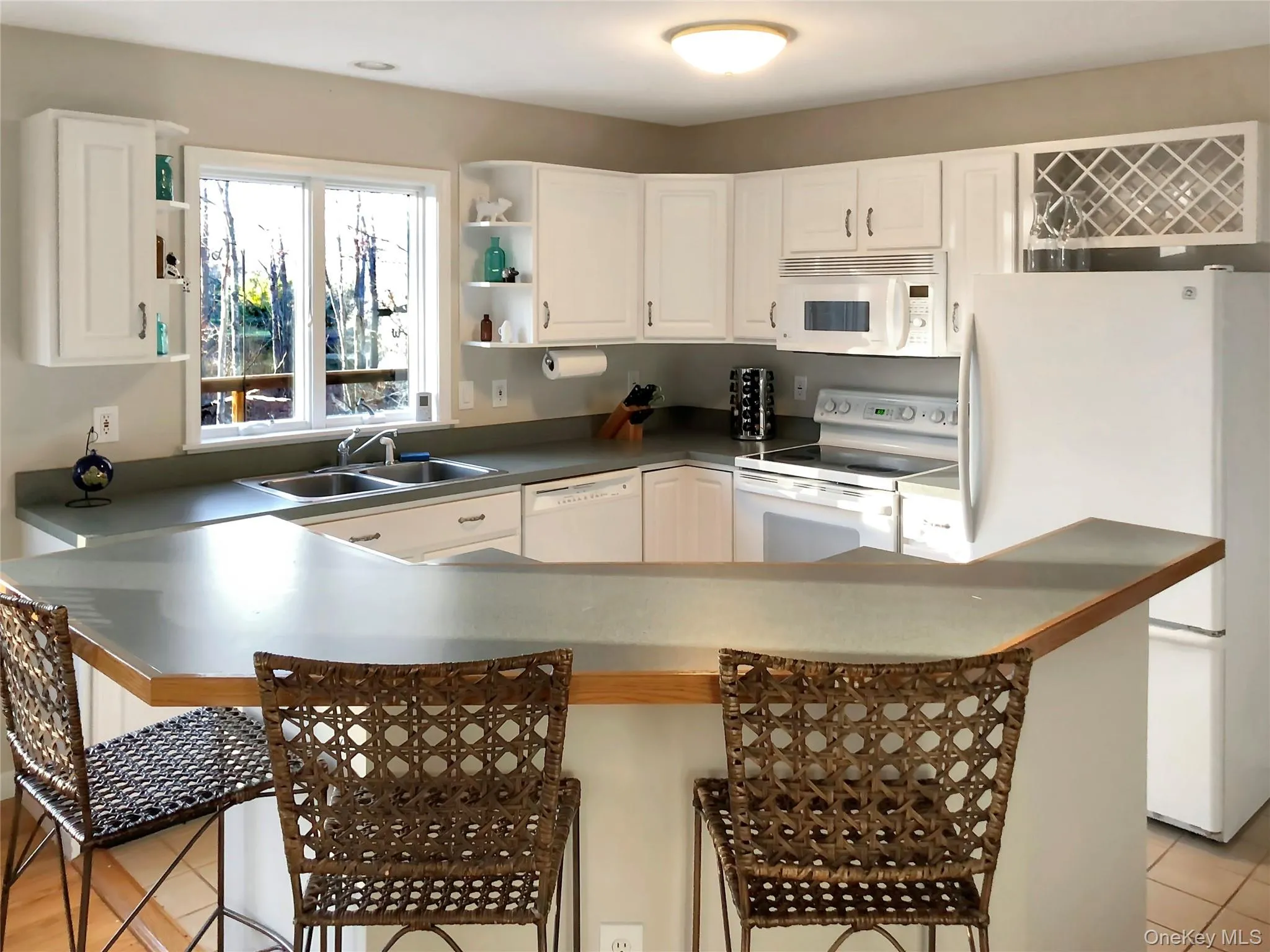 Kitchen featuring white appliances, white cabinetry, a breakfast bar area, open shelves, and dark countertops Kitchen featuring white appliances, white cabinetry, a breakfast bar area, open shelves, and dark countertops
