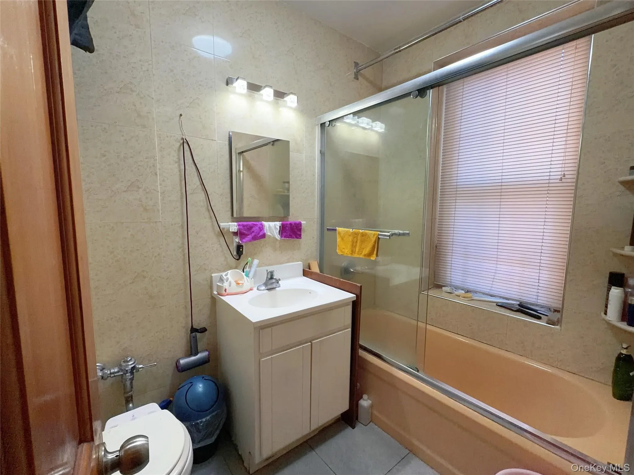 Bathroom featuring shower / bath combination with glass door, vanity, tile walls, and light tile patterned flooring Bathroom featuring shower / bath combination with glass door, vanity, tile walls, and light tile patterned flooring