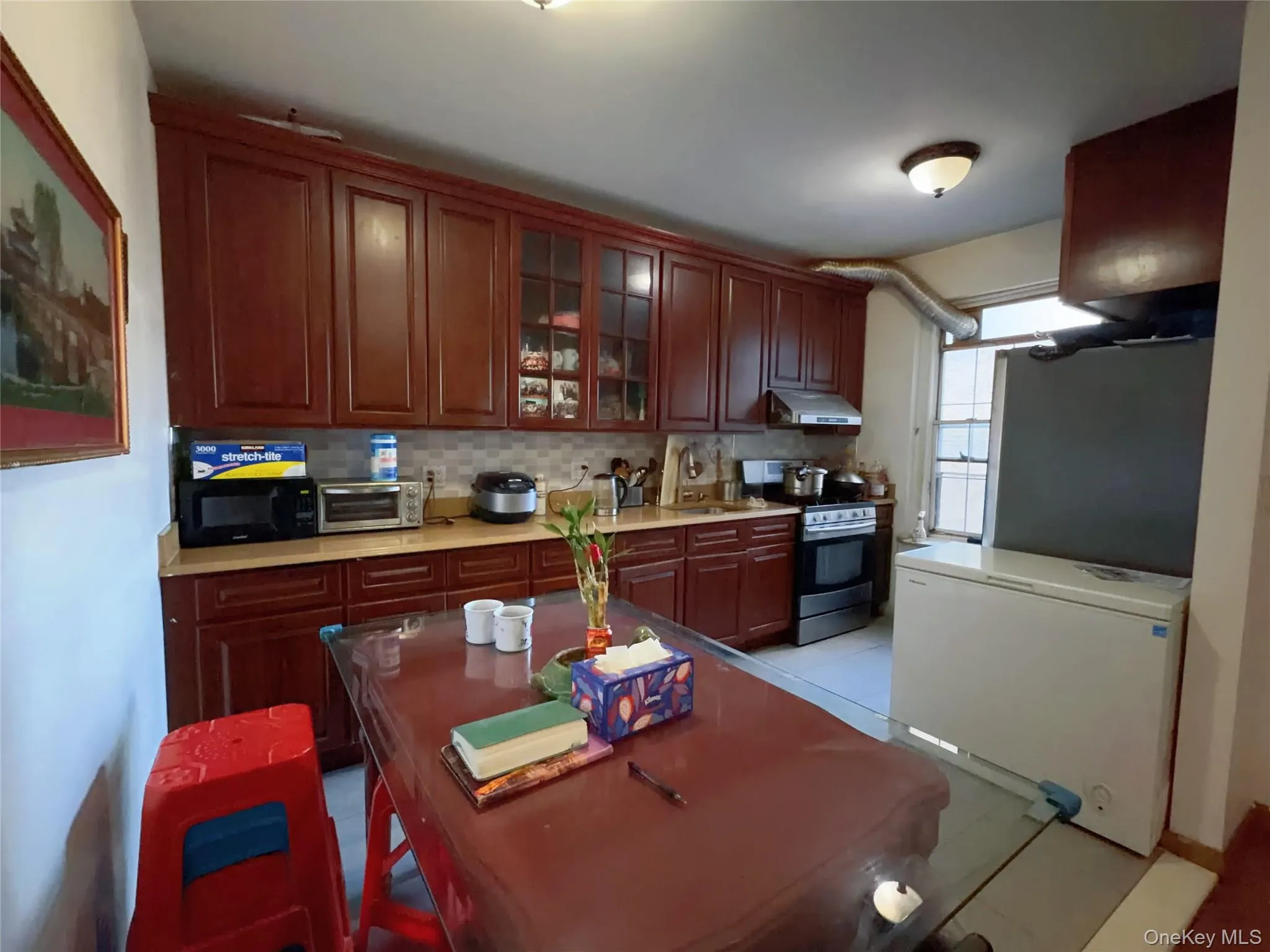 Kitchen featuring appliances with stainless steel finishes, decorative backsplash, glass insert cabinets, under cabinet range hood, and light tile patterned floors Kitchen featuring appliances with stainless steel finishes, decorative backsplash, glass insert cabinets, under cabinet range hood, and light tile patterned floors