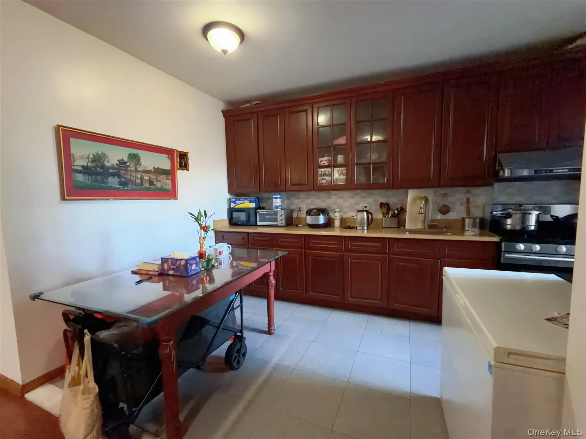 Kitchen featuring stainless steel range oven, tasteful backsplash, glass insert cabinets, extractor fan, and light tile patterned floors Kitchen featuring stainless steel range oven, tasteful backsplash, glass insert cabinets, extractor fan, and light tile patterned floors