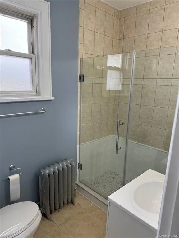 Full bath featuring a shower stall, radiator, vanity, and light tile patterned flooring Full bath featuring a shower stall, radiator, vanity, and light tile patterned flooring