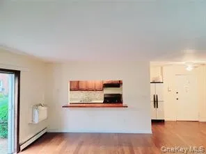 Unfurnished living room featuring wood finished floors, a baseboard heating unit, and a wall mounted air conditioner Unfurnished living room featuring wood finished floors, a baseboard heating unit, and a wall mounted air conditioner