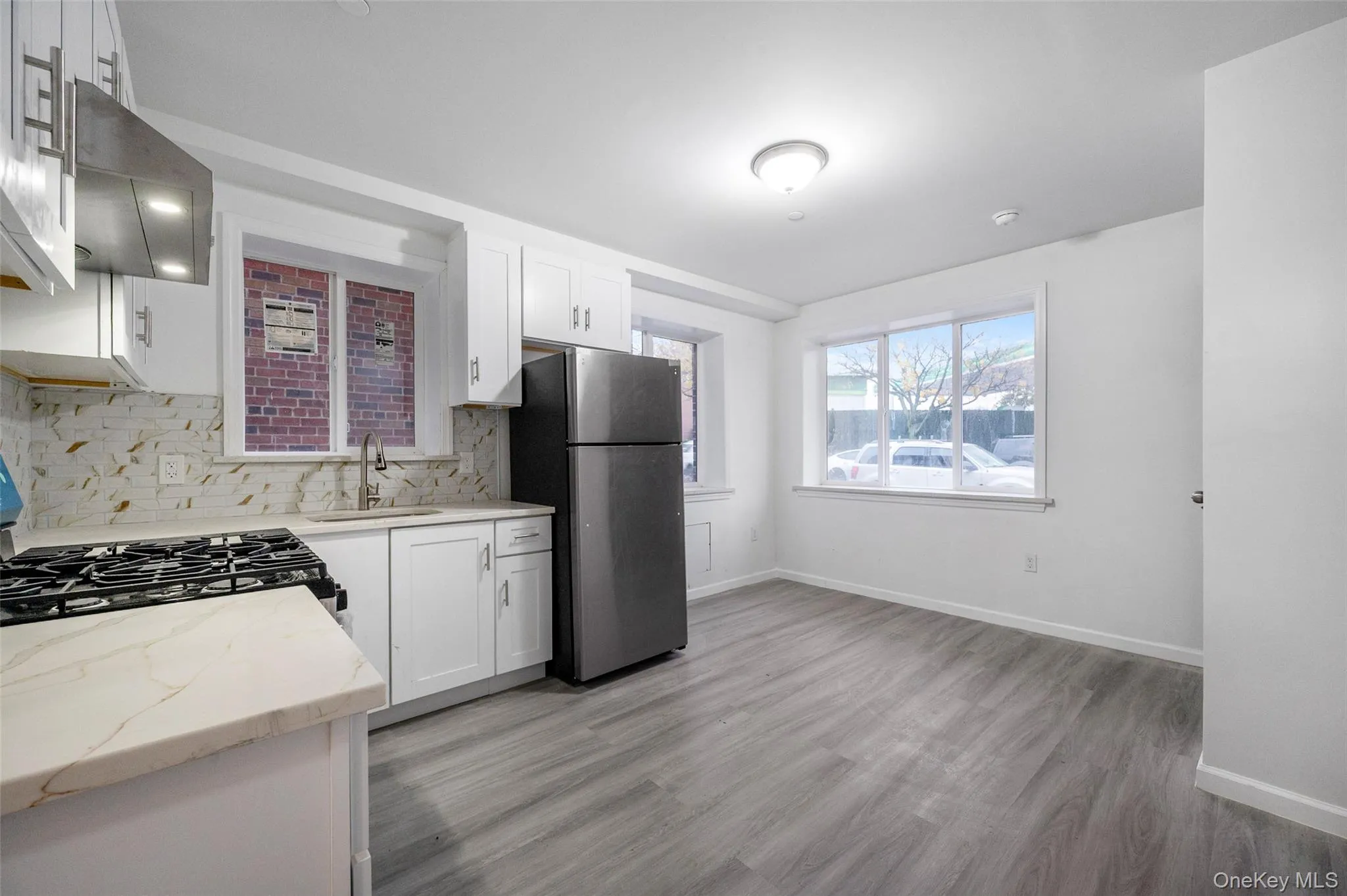 Kitchen with light stone counters, freestanding refrigerator, white cabinets, range hood, and decorative backsplash Kitchen with light stone counters, freestanding refrigerator, white cabinets, range hood, and decorative backsplash