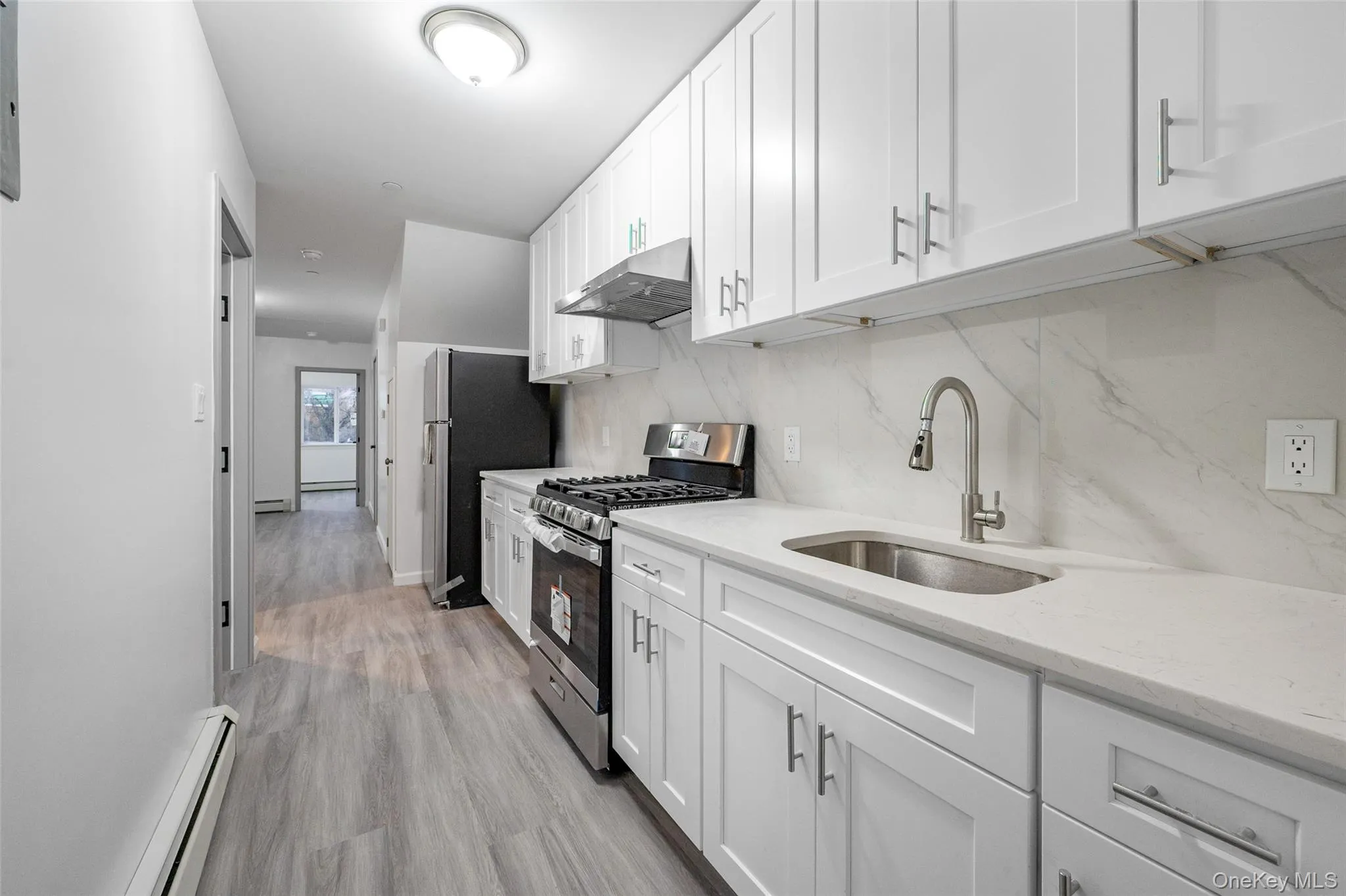 Kitchen with stainless steel appliances, a baseboard heating unit, white cabinetry, under cabinet range hood, and light stone counters Kitchen with stainless steel appliances, a baseboard heating unit, white cabinetry, under cabinet range hood, and light stone counters
