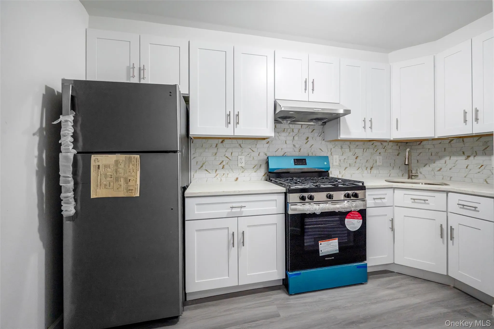 Kitchen featuring appliances with stainless steel finishes, white cabinetry, under cabinet range hood, light wood finished floors, and light stone counters Kitchen featuring appliances with stainless steel finishes, white cabinetry, under cabinet range hood, light wood finished floors, and light stone counters