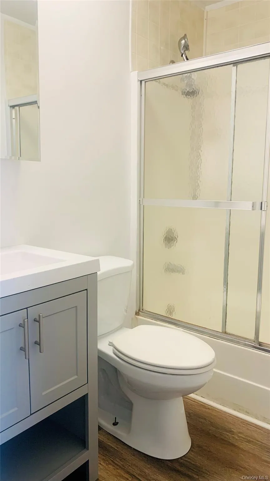 Bathroom featuring vanity, shower / bath combination with glass door, and dark wood-style floors Bathroom featuring vanity, shower / bath combination with glass door, and dark wood-style floors