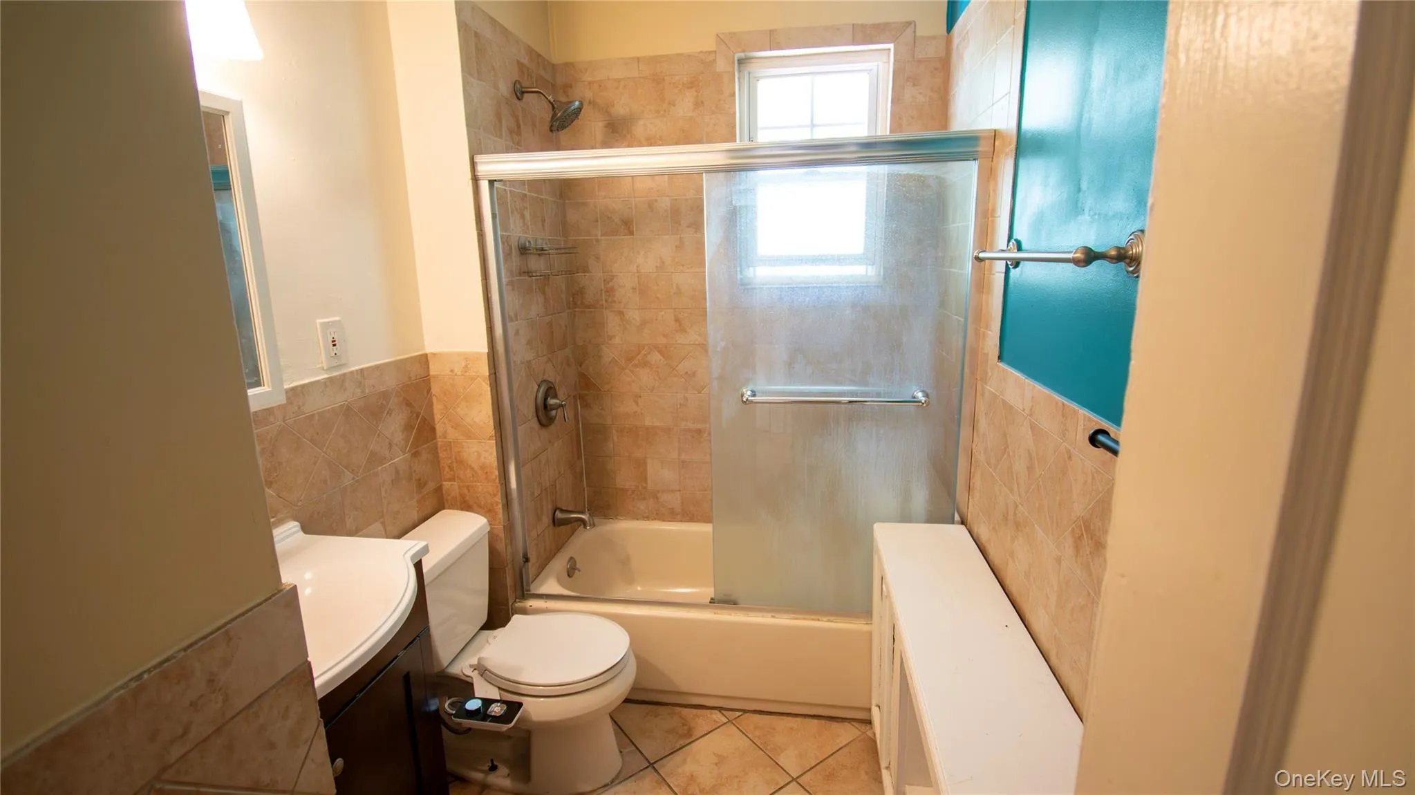 Full bathroom with vanity, enclosed tub / shower combo, tile walls, tile patterned flooring, and wainscoting Full bathroom with vanity, enclosed tub / shower combo, tile walls, tile patterned flooring, and wainscoting