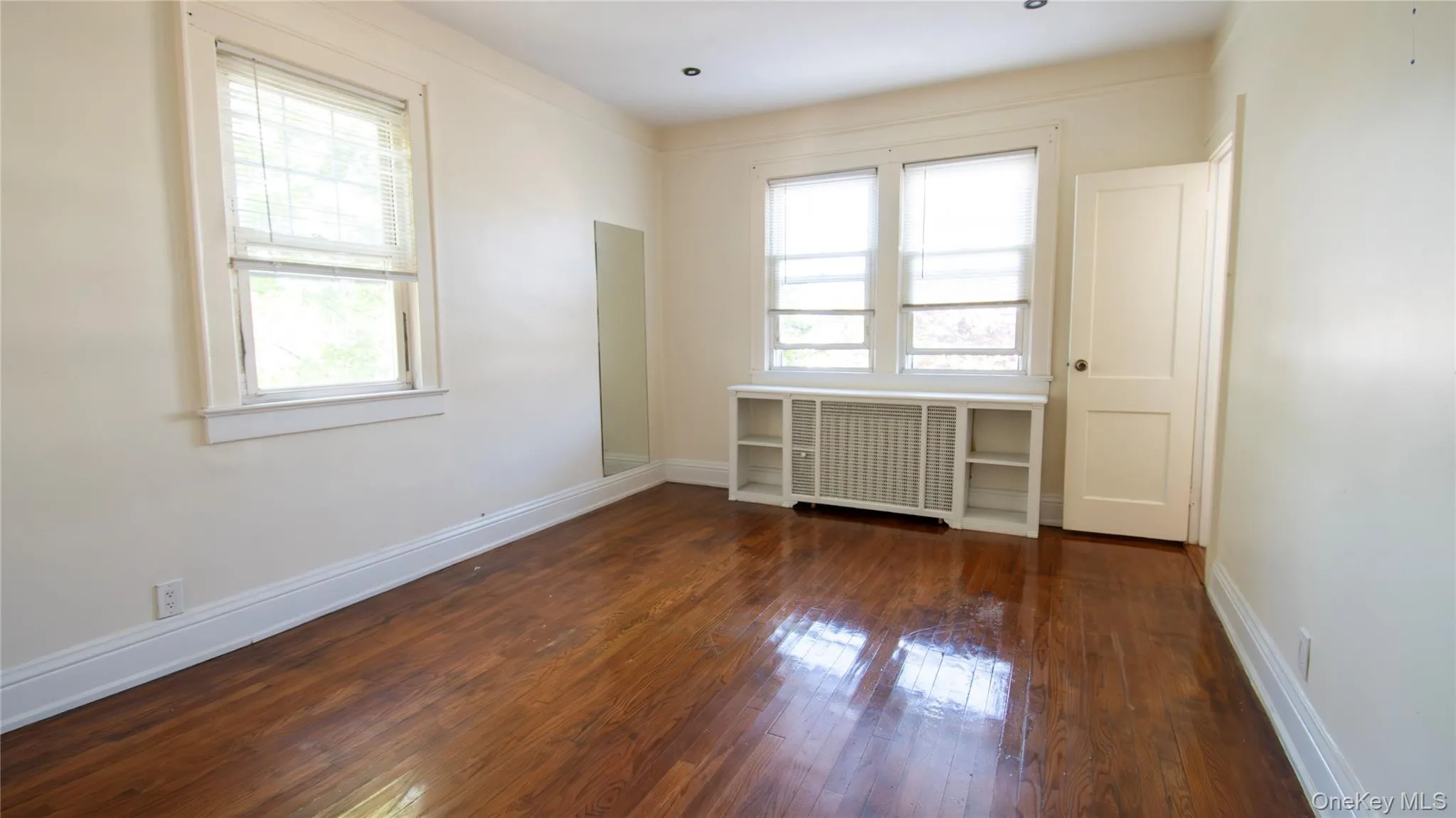Empty room with healthy amount of natural light, dark wood-style floors, and radiator heating unit Empty room with healthy amount of natural light, dark wood-style floors, and radiator heating unit