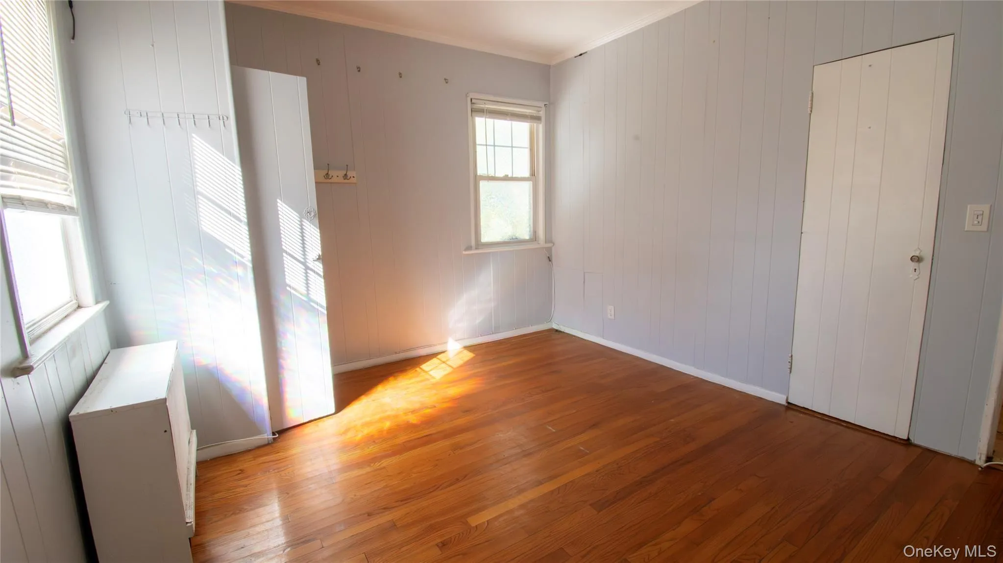 Spare room featuring wood walls, crown molding, and hardwood / wood-style floors Spare room featuring wood walls, crown molding, and hardwood / wood-style floors