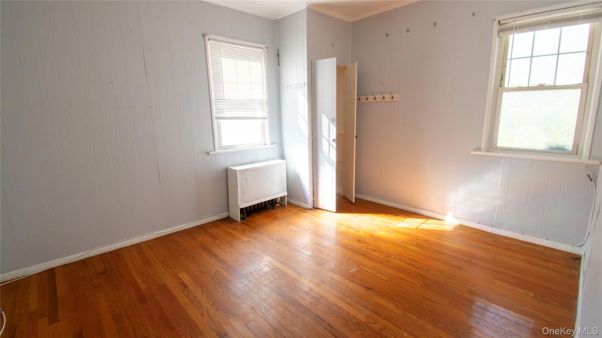 Empty room with radiator heating unit, hardwood / wood-style flooring, ornamental molding, wooden walls, and plenty of natural light Empty room with radiator heating unit, hardwood / wood-style flooring, ornamental molding, wooden walls, and plenty of natural light