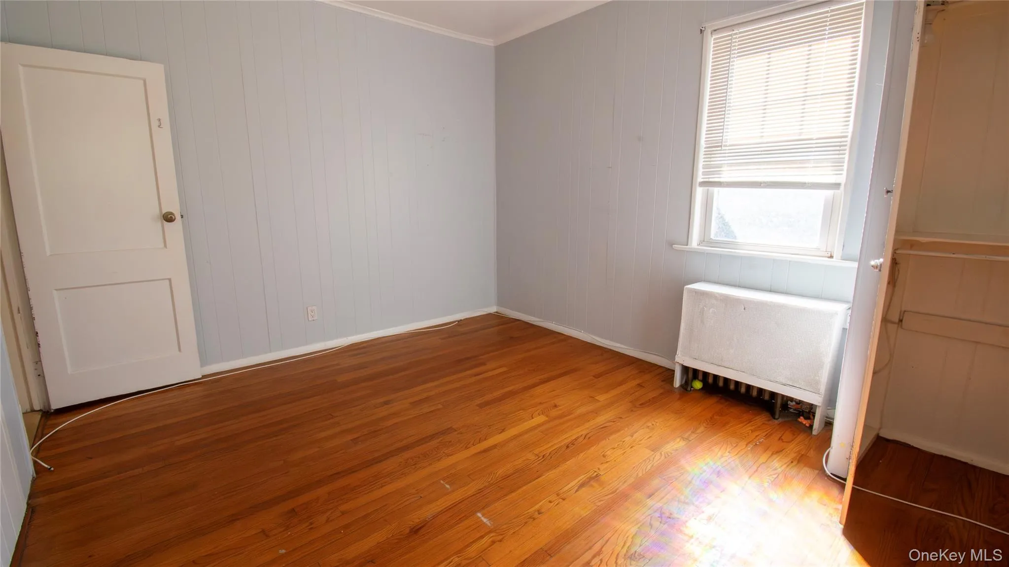 Spare room featuring light wood finished floors, wood walls, ornamental molding, and radiator Spare room featuring light wood finished floors, wood walls, ornamental molding, and radiator