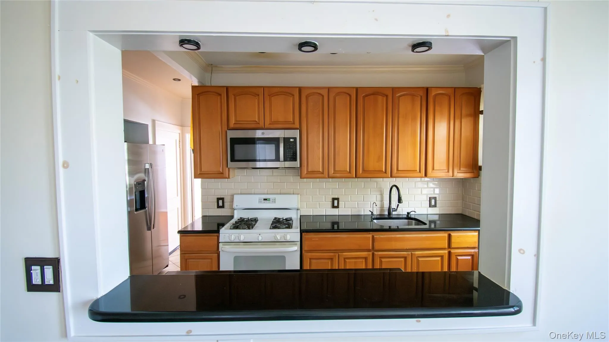 Kitchen featuring stainless steel appliances, brown cabinetry, crown molding, and decorative backsplash Kitchen featuring stainless steel appliances, brown cabinetry, crown molding, and decorative backsplash