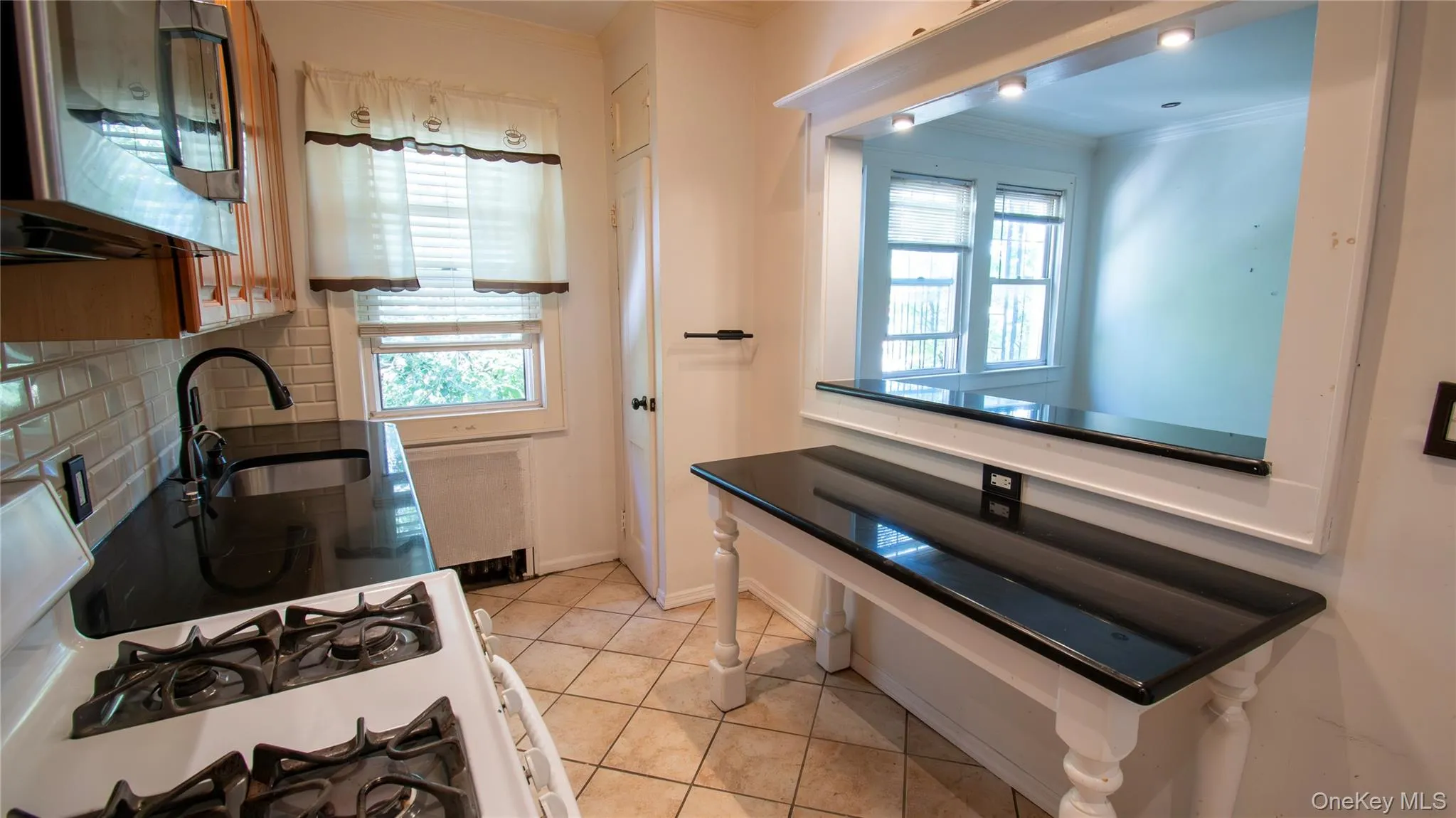 Kitchen with white gas range oven, crown molding, tasteful backsplash, stainless steel microwave, and light tile patterned floors Kitchen with white gas range oven, crown molding, tasteful backsplash, stainless steel microwave, and light tile patterned floors