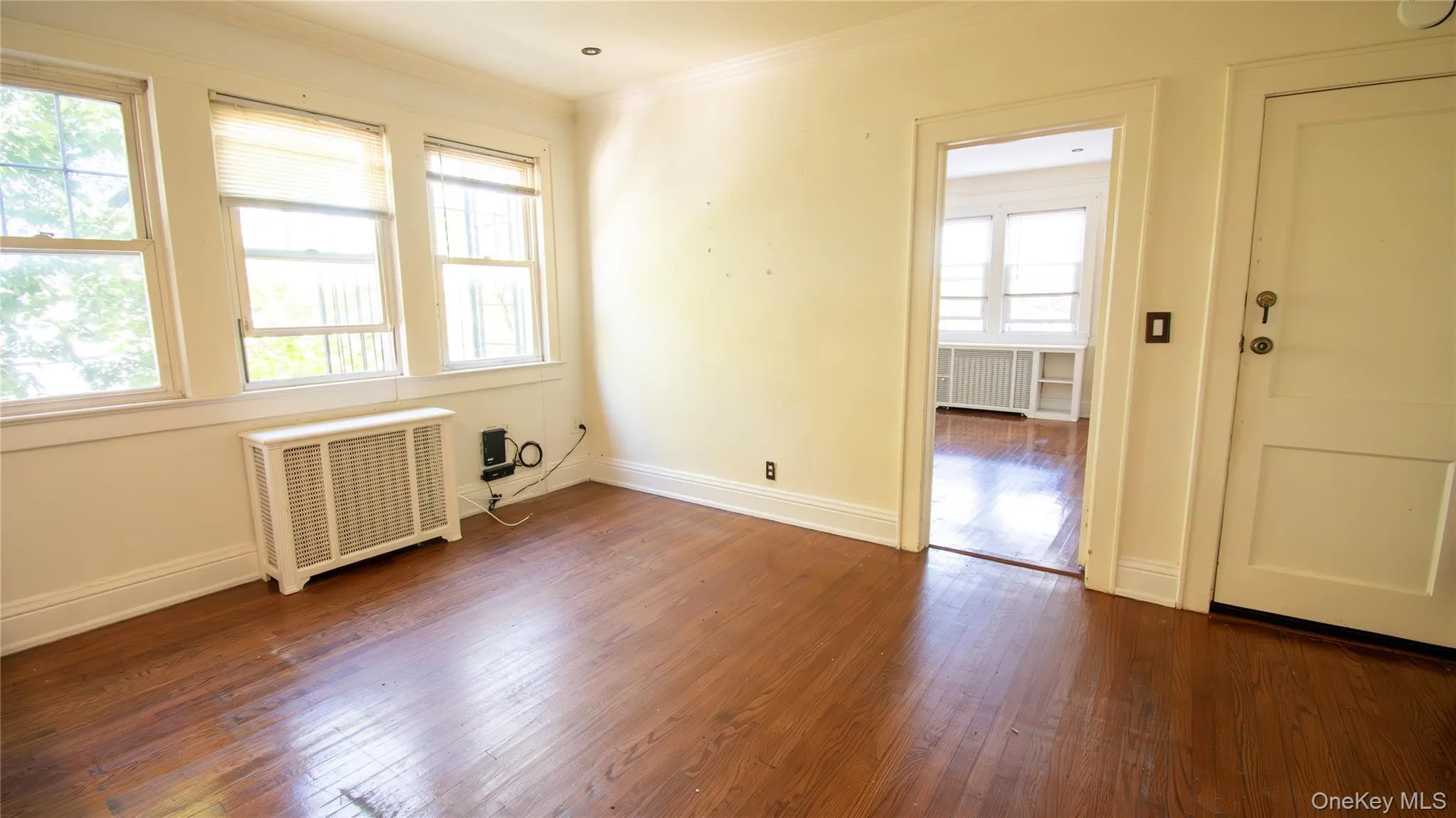 Empty room with radiator heating unit, dark wood-style flooring, and crown molding Empty room with radiator heating unit, dark wood-style flooring, and crown molding