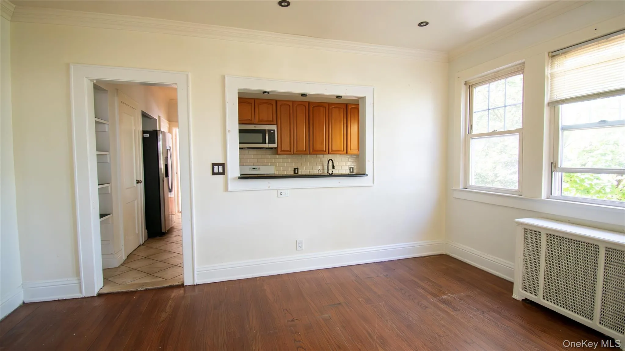 Unfurnished dining area featuring radiator heating unit, dark wood-style floors, and ornamental molding Unfurnished dining area featuring radiator heating unit, dark wood-style floors, and ornamental molding