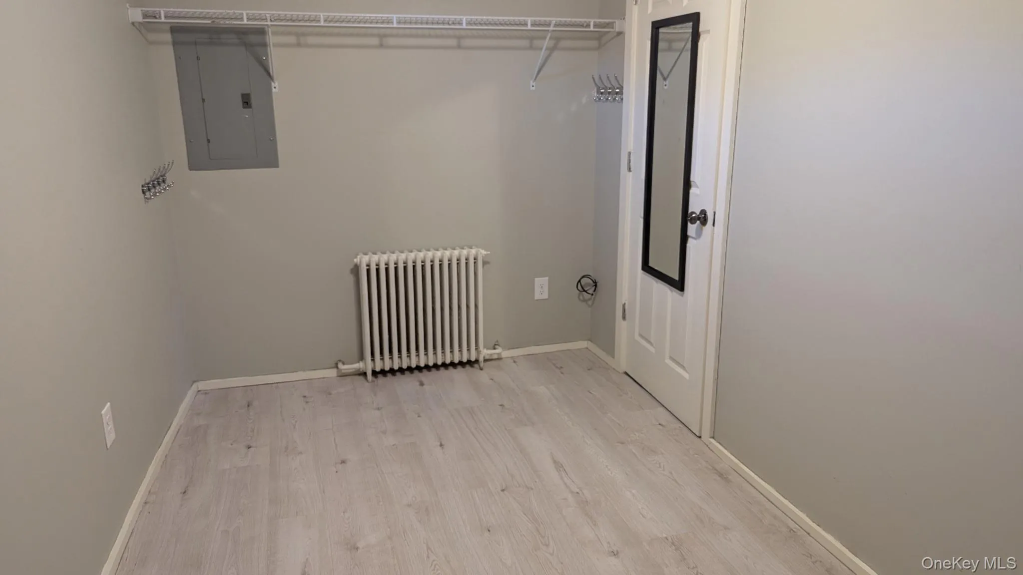 Laundry room with radiator heating unit, electric panel, and light wood finished floors Laundry room with radiator heating unit, electric panel, and light wood finished floors