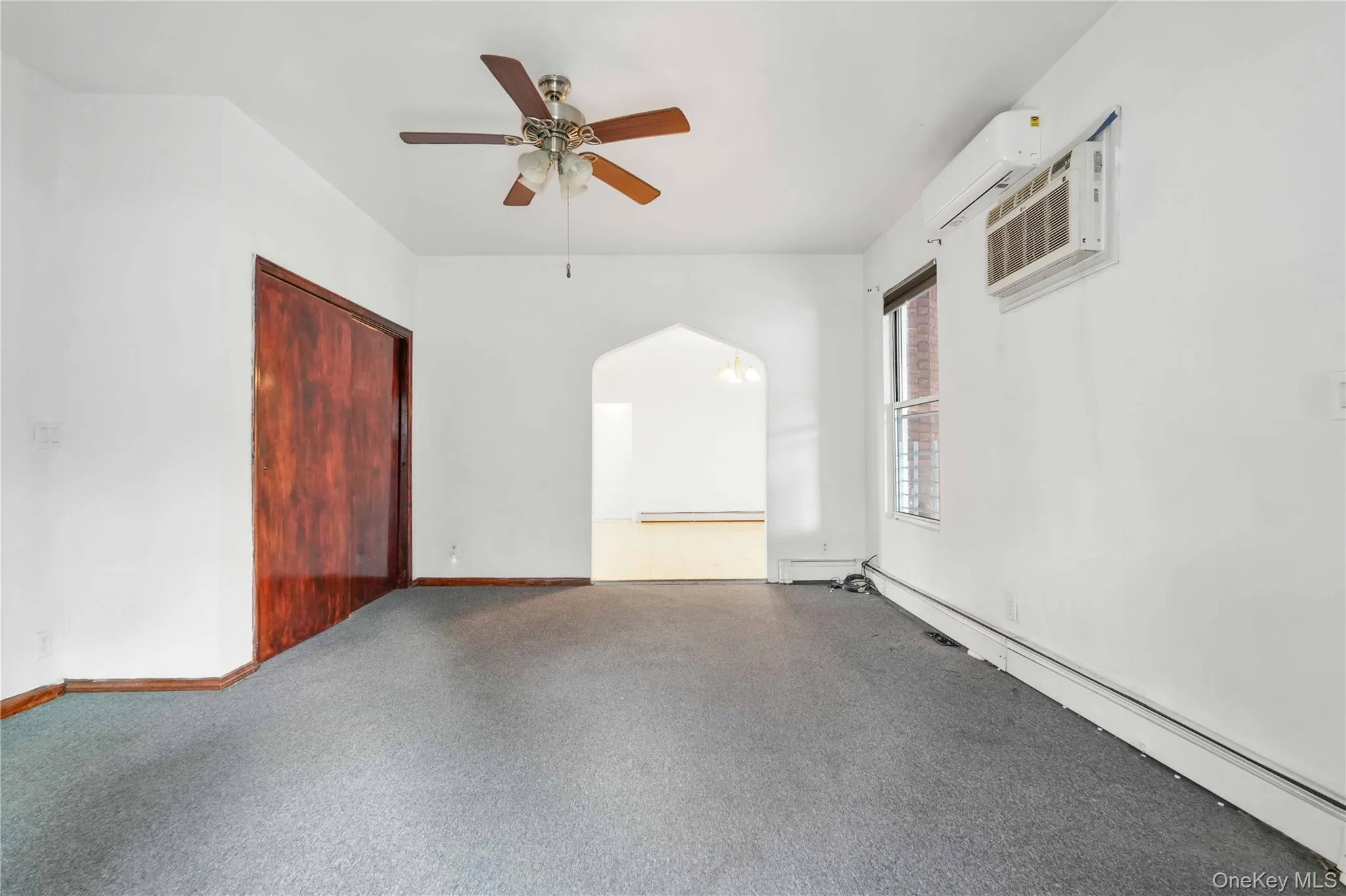 Unfurnished room featuring a baseboard radiator, a wall unit AC, arched walkways, and a ceiling fan Unfurnished room featuring a baseboard radiator, a wall unit AC, arched walkways, and a ceiling fan