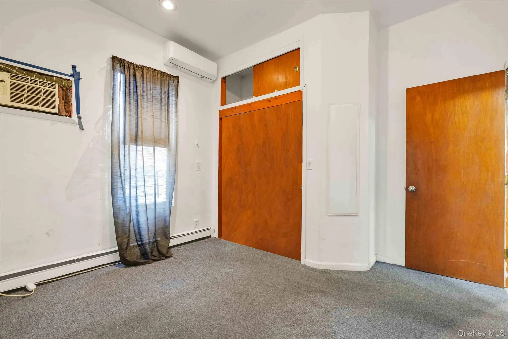 Unfurnished bedroom featuring a baseboard heating unit, a closet, a wall mounted AC, an AC wall unit, and carpet floors Unfurnished bedroom featuring a baseboard heating unit, a closet, a wall mounted AC, an AC wall unit, and carpet floors