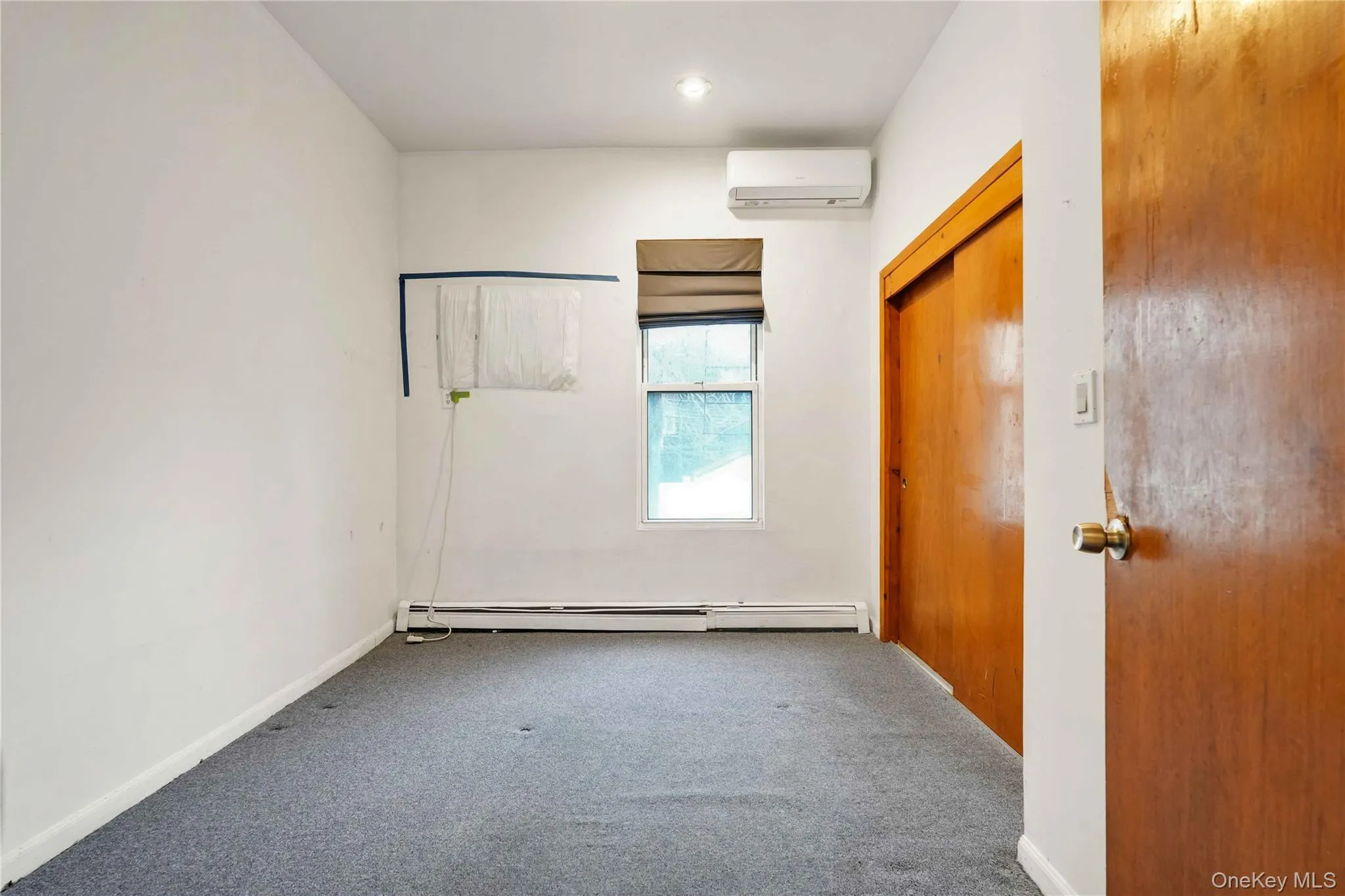 Carpeted spare room with a wall mounted air conditioner and a baseboard heating unit Carpeted spare room with a wall mounted air conditioner and a baseboard heating unit