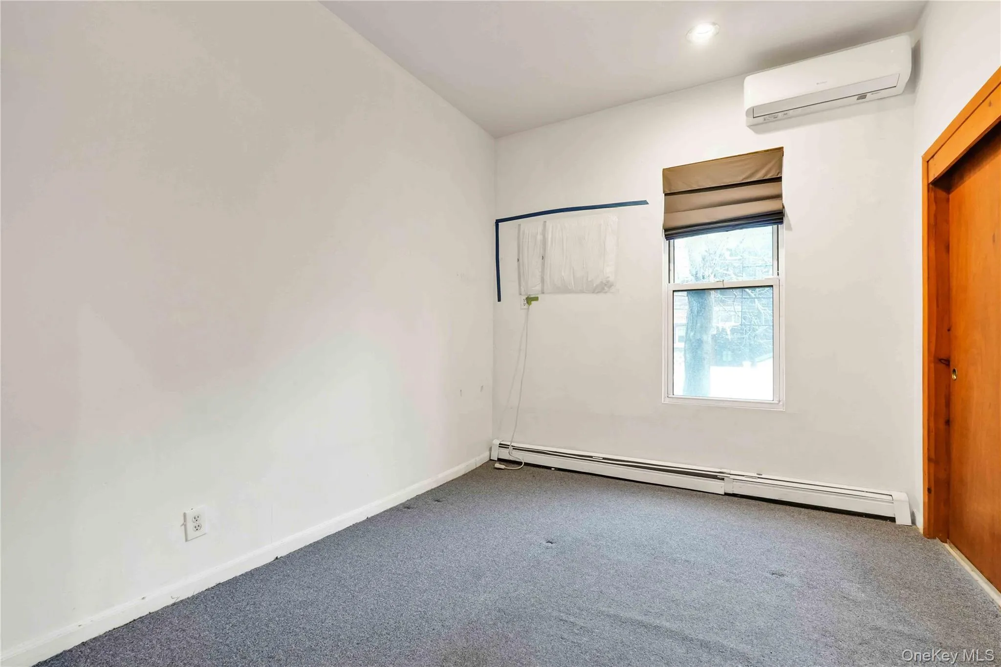 Unfurnished bedroom featuring baseboard heating, carpet, and a wall mounted air conditioner Unfurnished bedroom featuring baseboard heating, carpet, and a wall mounted air conditioner