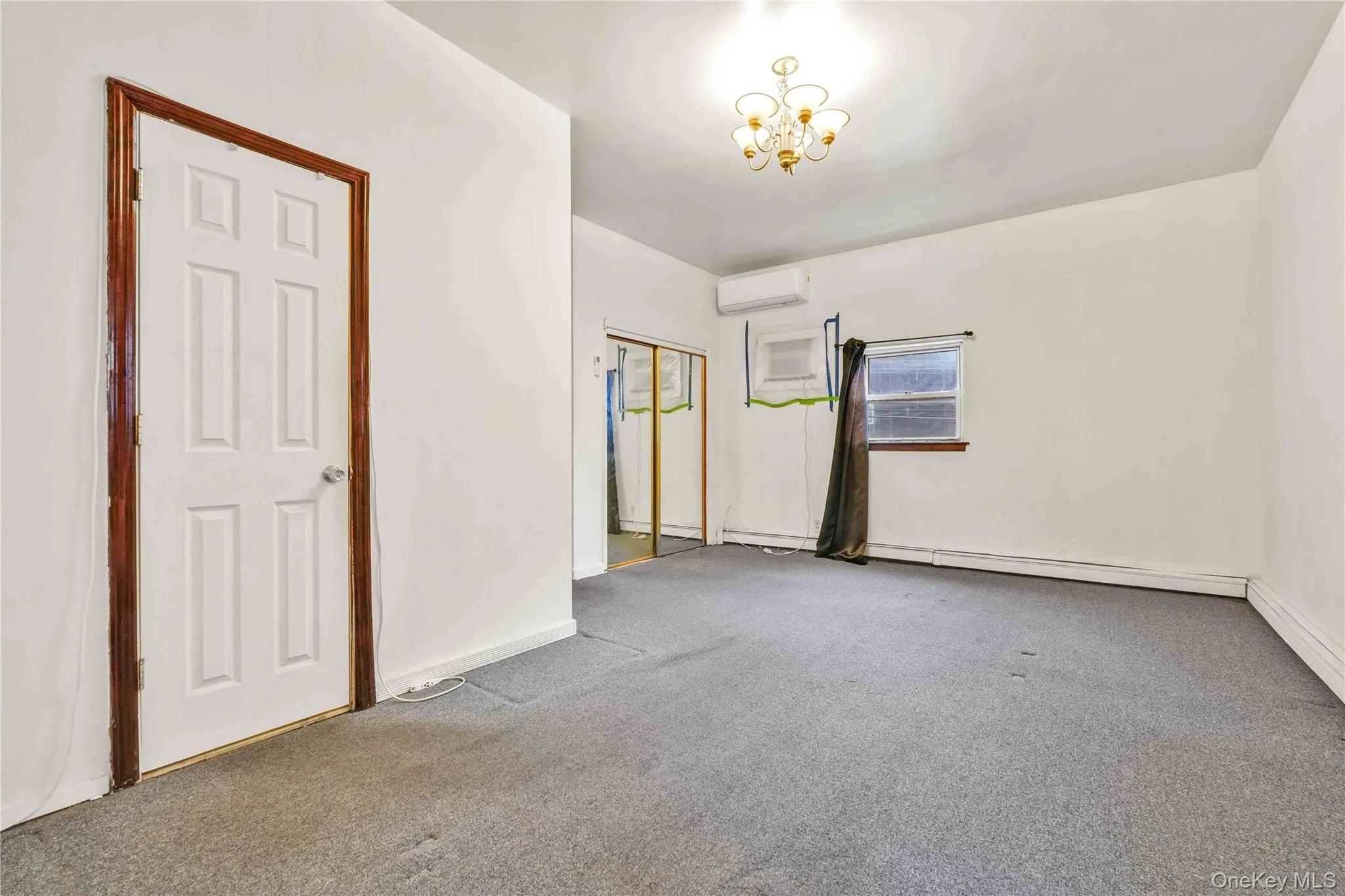 Spare room with carpet flooring, a wall mounted air conditioner, a chandelier, and a baseboard radiator Spare room with carpet flooring, a wall mounted air conditioner, a chandelier, and a baseboard radiator