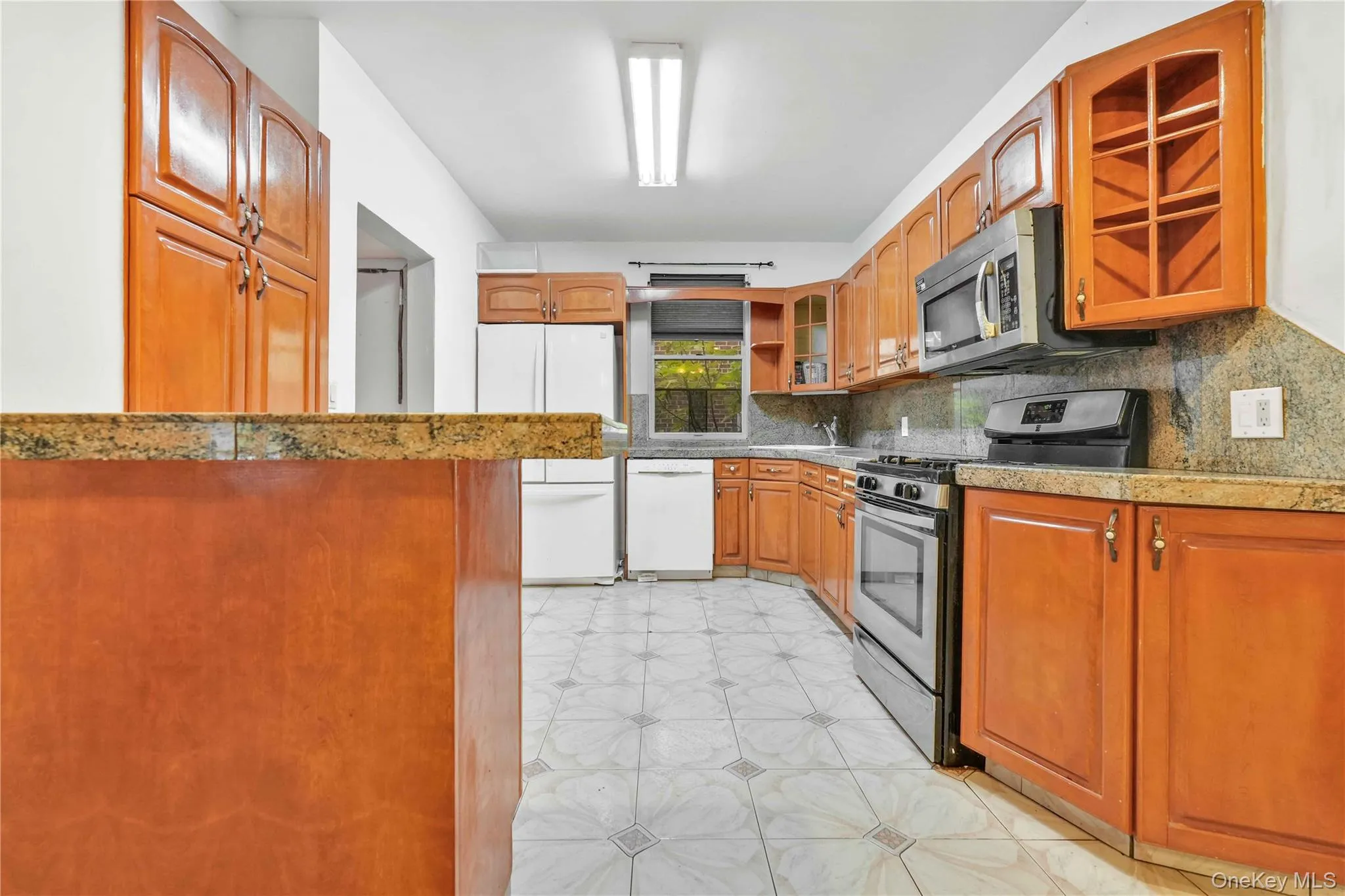 Kitchen featuring appliances with stainless steel finishes, backsplash, glass insert cabinets, light floors, and light stone countertops Kitchen featuring appliances with stainless steel finishes, backsplash, glass insert cabinets, light floors, and light stone countertops