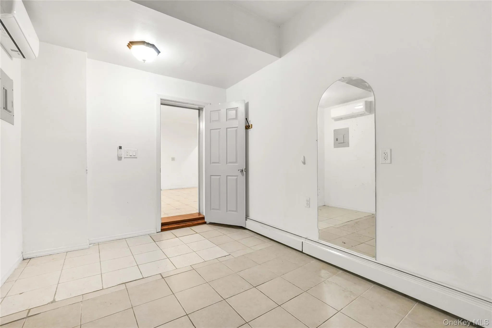 Empty room featuring a baseboard heating unit, a wall mounted air conditioner, arched walkways, and light tile patterned floors Empty room featuring a baseboard heating unit, a wall mounted air conditioner, arched walkways, and light tile patterned floors