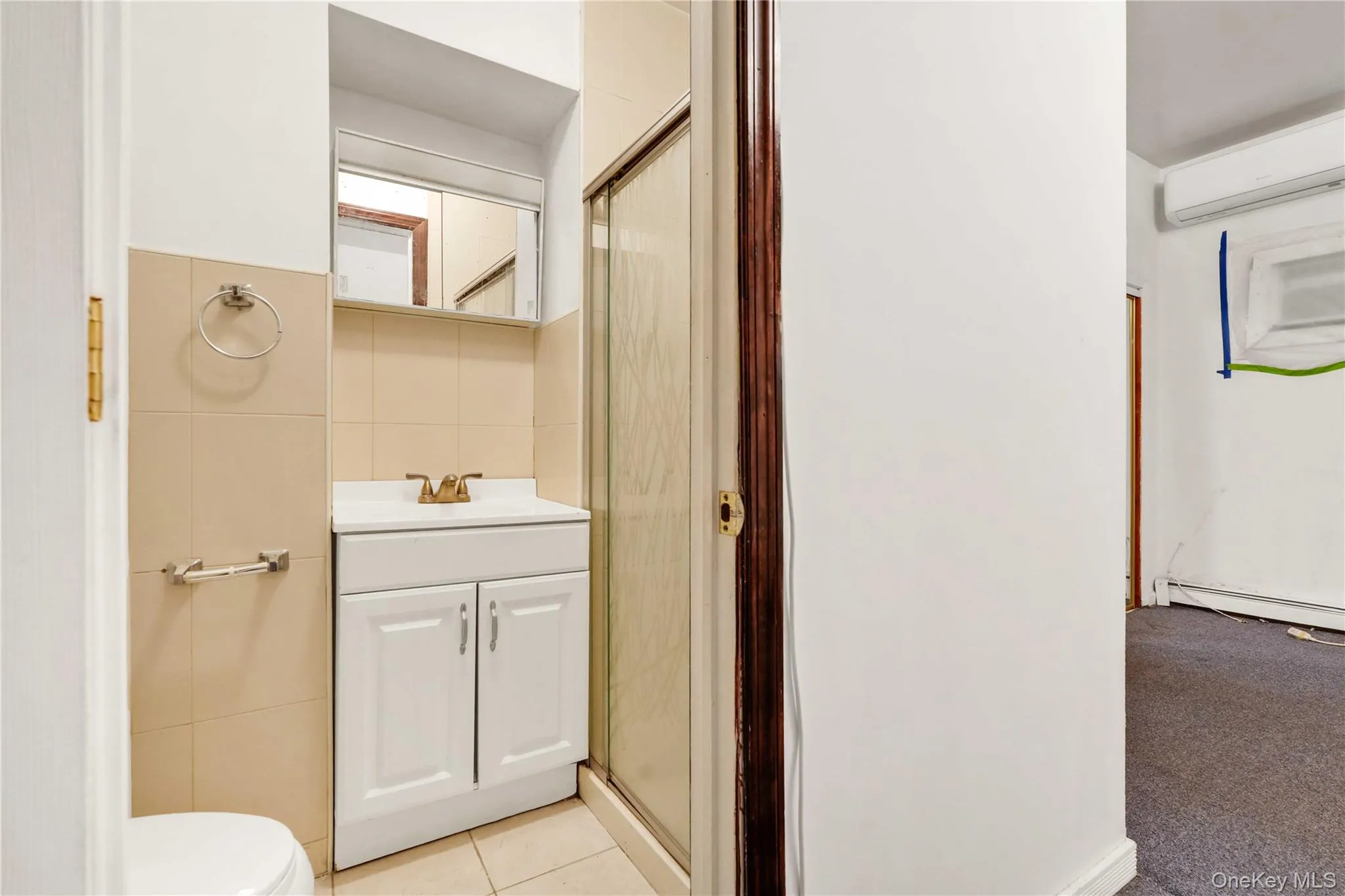 Bathroom featuring a stall shower, vanity, a wall unit AC, tile walls, and light tile patterned flooring Bathroom featuring a stall shower, vanity, a wall unit AC, tile walls, and light tile patterned flooring