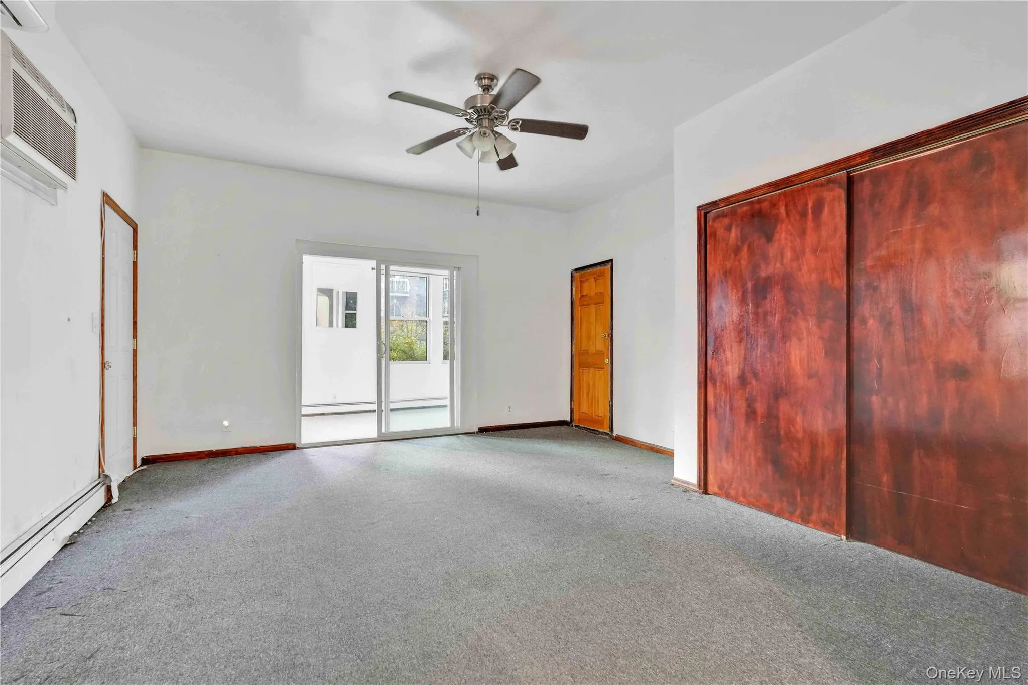 Unfurnished bedroom with carpet floors, access to exterior, a ceiling fan, a closet, and a wall unit AC Unfurnished bedroom with carpet floors, access to exterior, a ceiling fan, a closet, and a wall unit AC