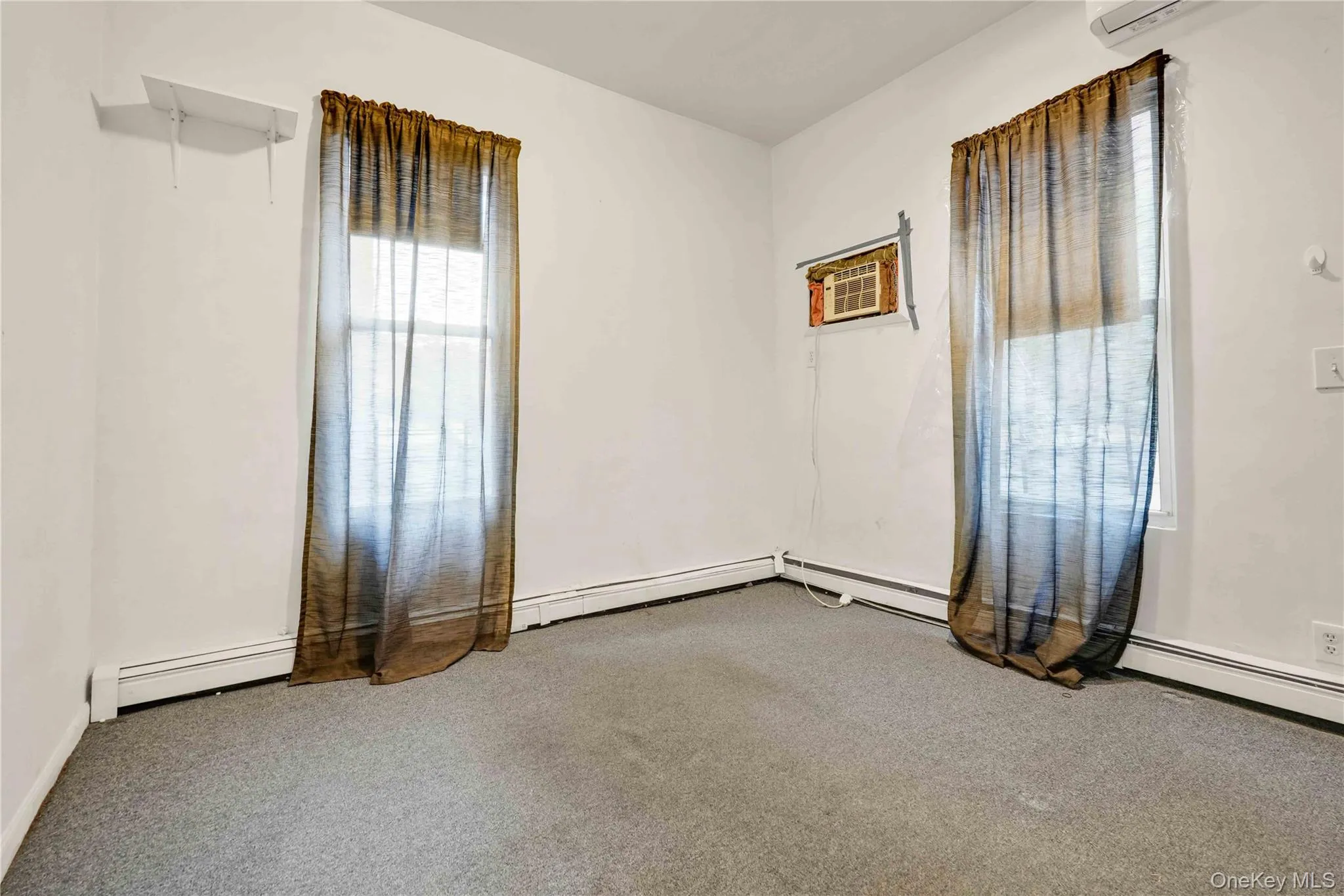Carpeted empty room featuring baseboard heating and a wall mounted AC Carpeted empty room featuring baseboard heating and a wall mounted AC