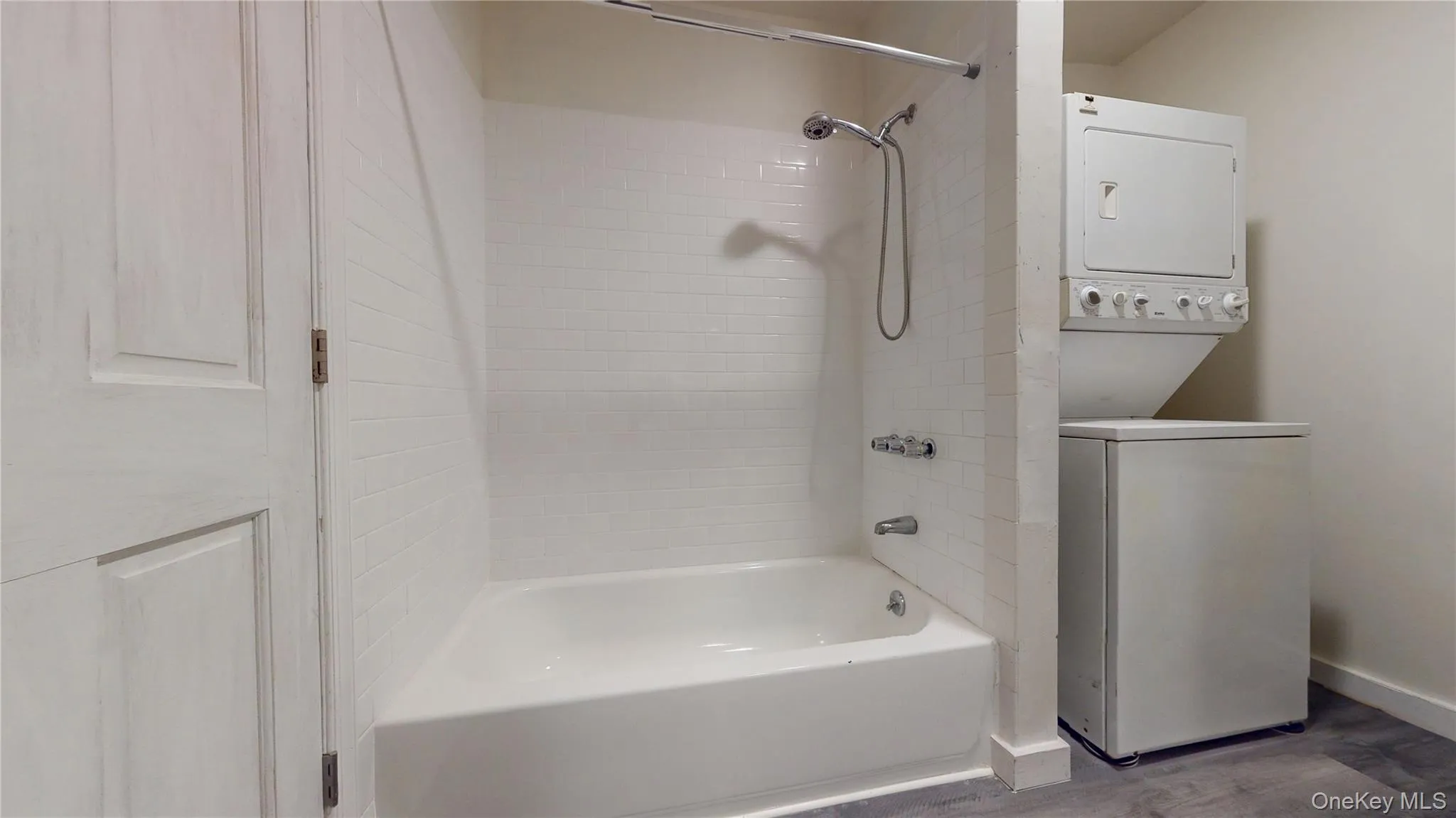 Full bath with shower / washtub combination, stacked washer / dryer, and wood finished floors Full bath with shower / washtub combination, stacked washer / dryer, and wood finished floors