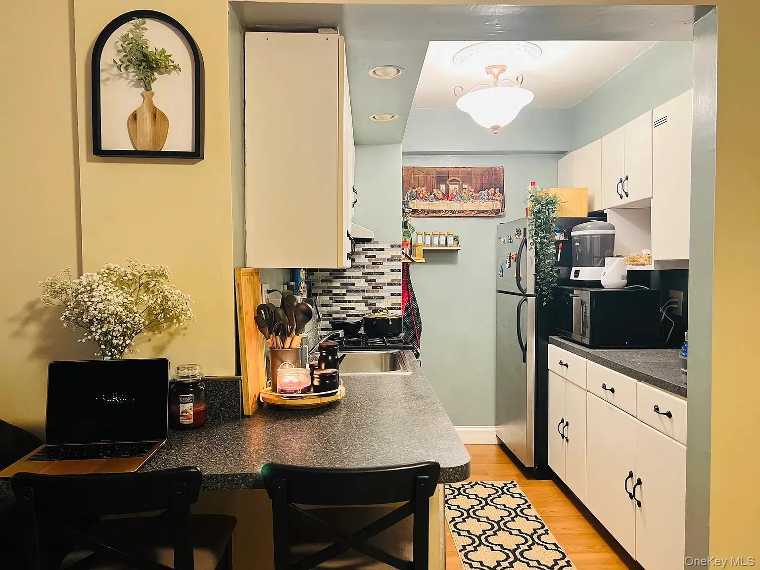 Kitchen featuring dark countertops, white cabinetry, tasteful backsplash, stainless steel microwave, and light wood-style floors Kitchen featuring dark countertops, white cabinetry, tasteful backsplash, stainless steel microwave, and light wood-style floors