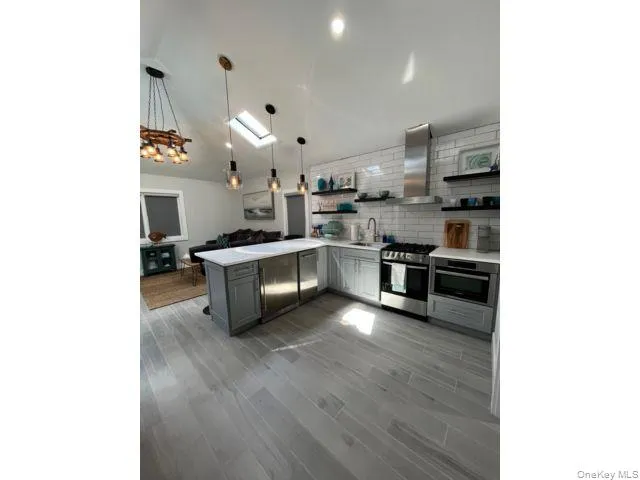 Kitchen featuring a peninsula, open shelves, pendant lighting, appliances with stainless steel finishes, and dark wood-type flooring Kitchen featuring a peninsula, open shelves, pendant lighting, appliances with stainless steel finishes, and dark wood-type flooring