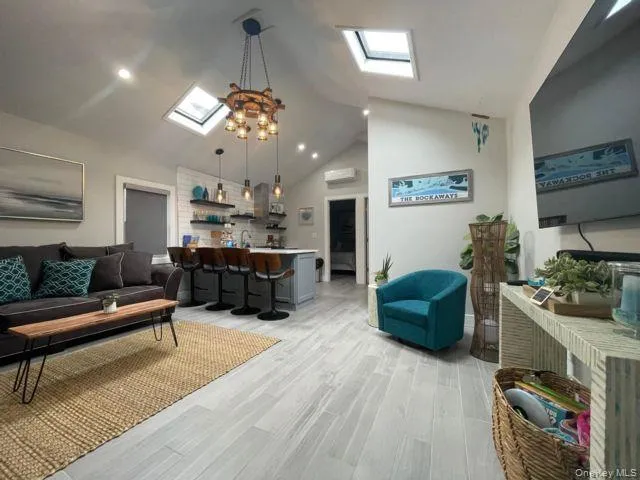 Living room featuring a skylight, light wood-style flooring, high vaulted ceiling, an AC wall unit, and recessed lighting Living room featuring a skylight, light wood-style flooring, high vaulted ceiling, an AC wall unit, and recessed lighting
