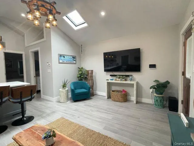 Living room with a skylight, high vaulted ceiling, wood finished floors, and recessed lighting Living room with a skylight, high vaulted ceiling, wood finished floors, and recessed lighting