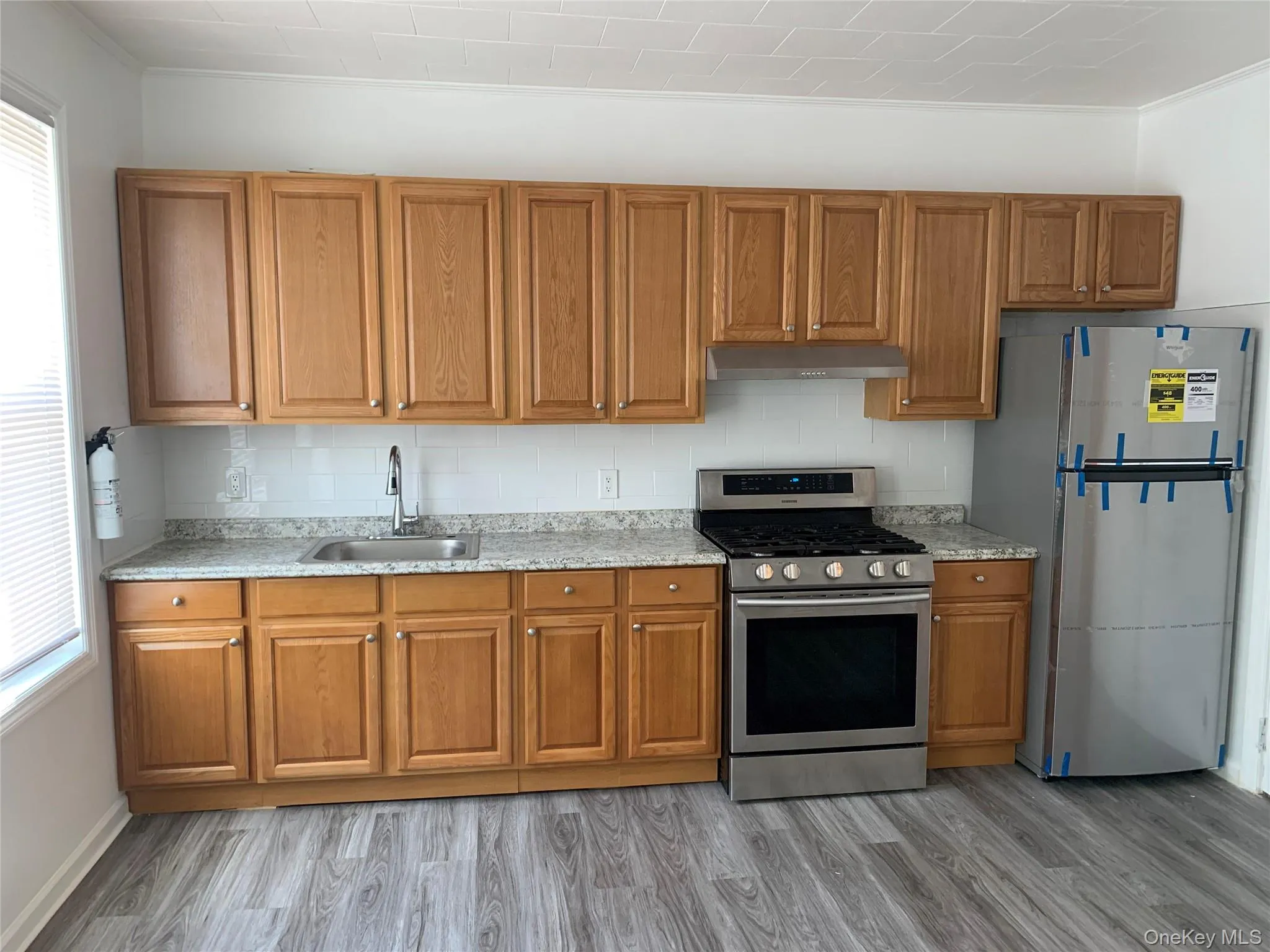 Kitchen with appliances with stainless steel finishes, brown cabinetry, light stone counters, and under cabinet range hood Kitchen with appliances with stainless steel finishes, brown cabinetry, light stone counters, and under cabinet range hood