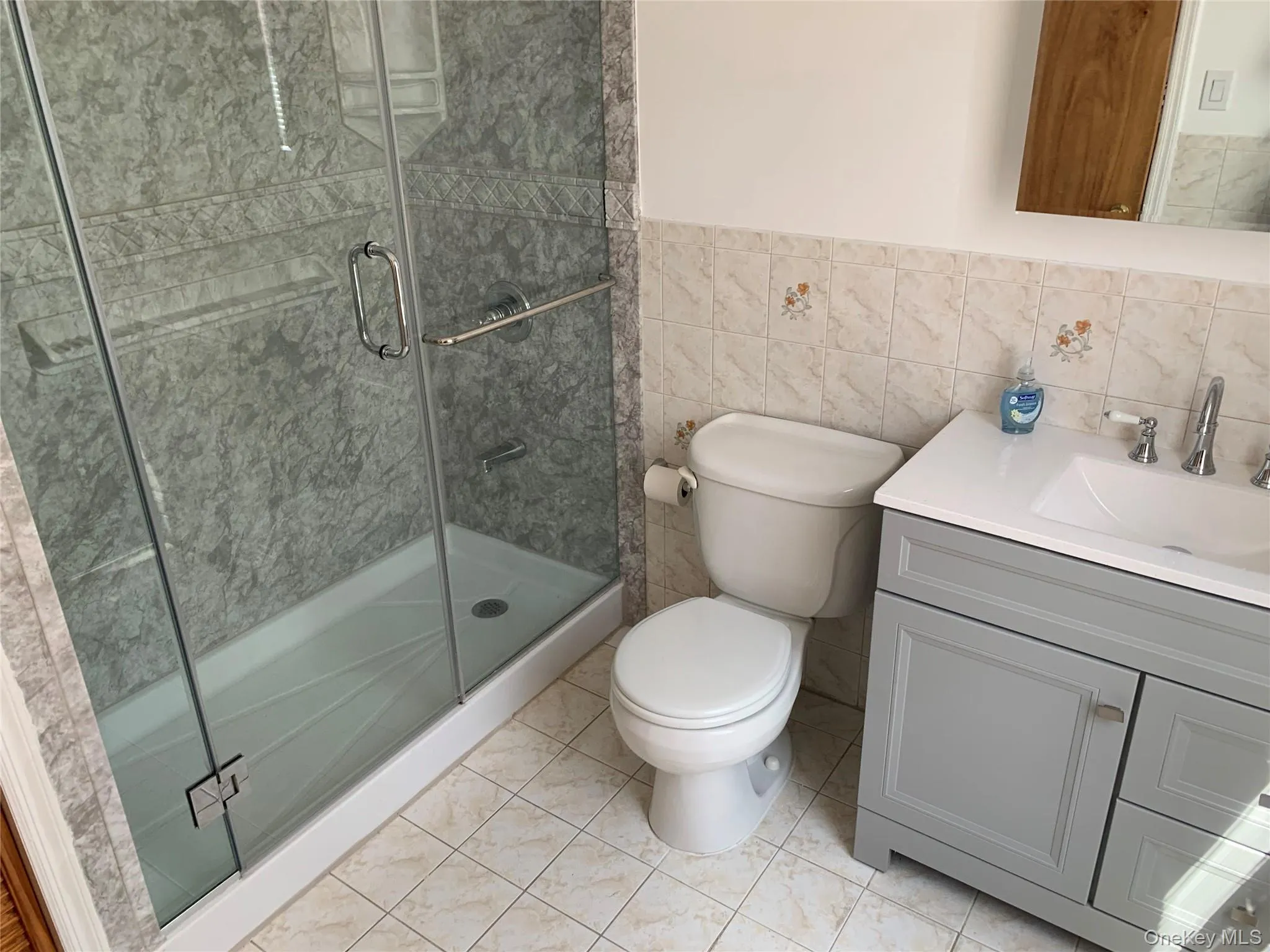 Full bath featuring vanity, tile walls, a shower stall, light tile patterned floors, and a wainscoted wall Full bath featuring vanity, tile walls, a shower stall, light tile patterned floors, and a wainscoted wall