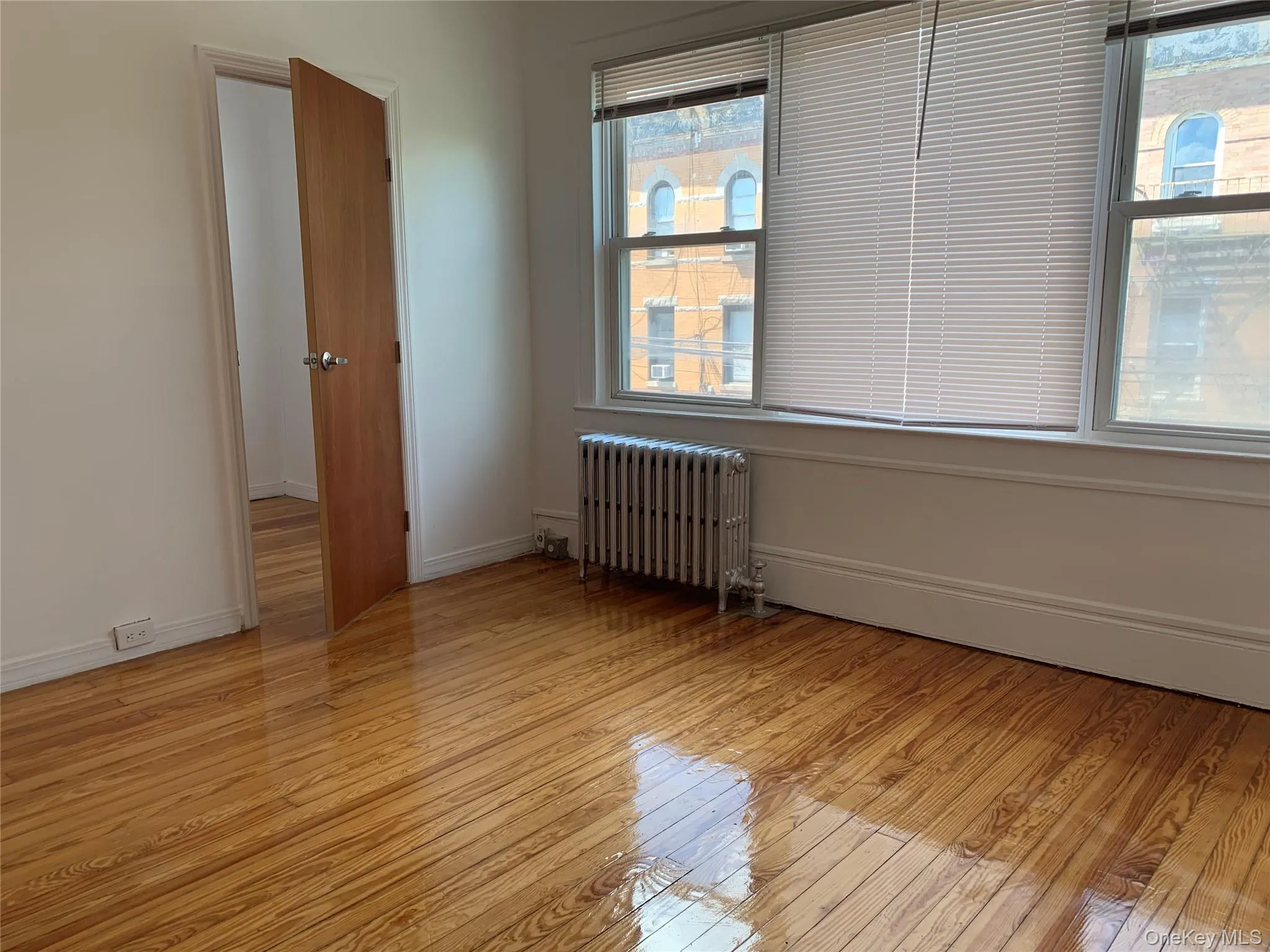 Unfurnished room featuring radiator and light wood finished floors Unfurnished room featuring radiator and light wood finished floors